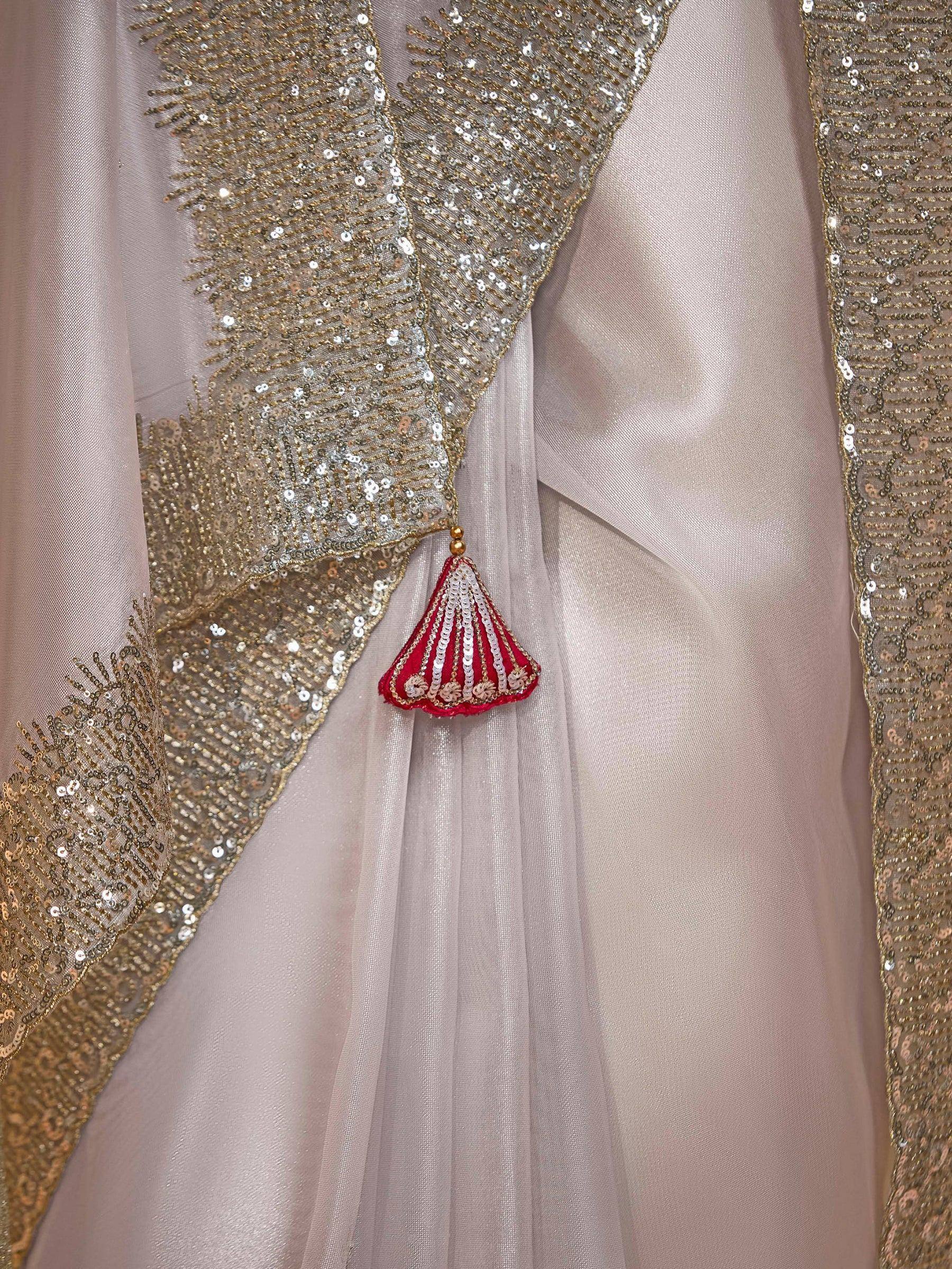 Elegant beige ethnic gown with gold sequin border and red tassel detail, perfect for Indian weddings.