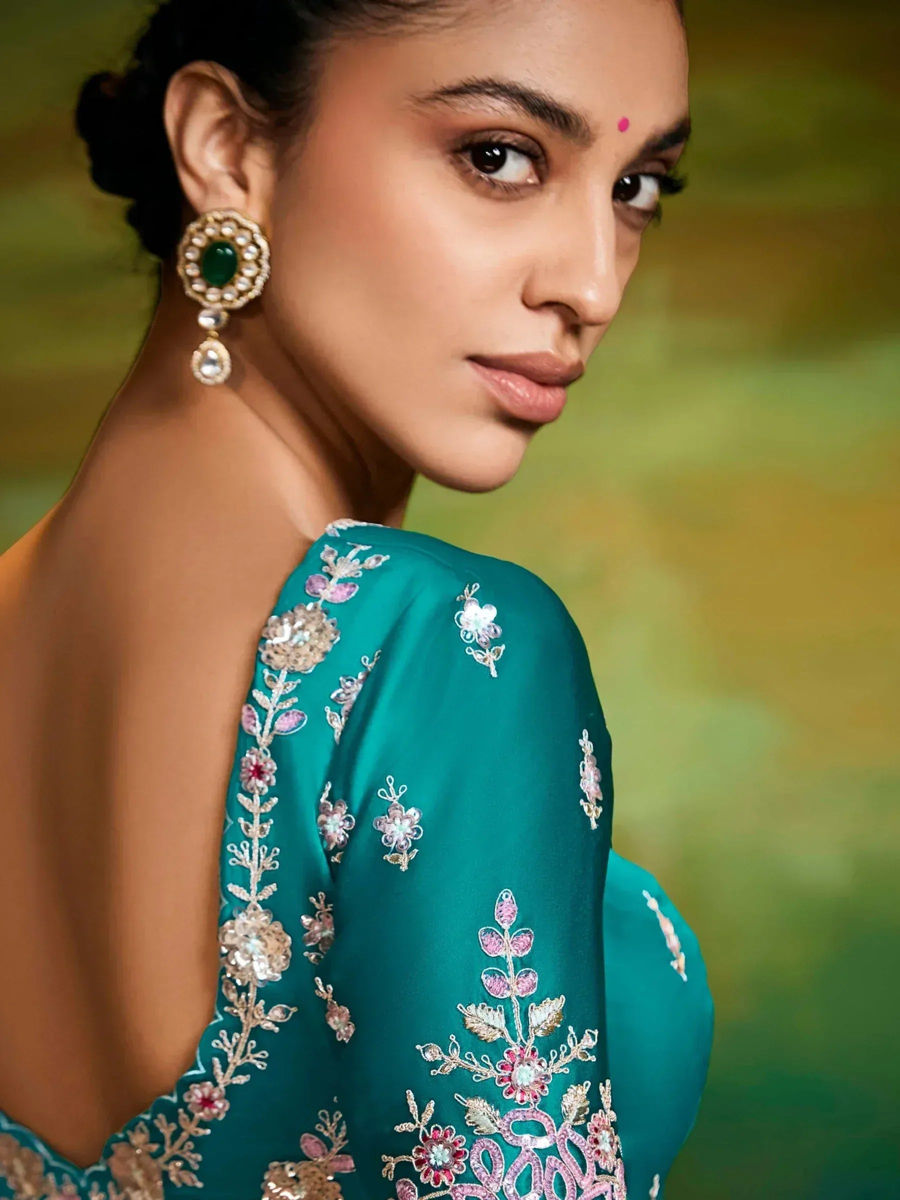 Woman in teal embroidered ethnic gown with floral details and green statement earrings
