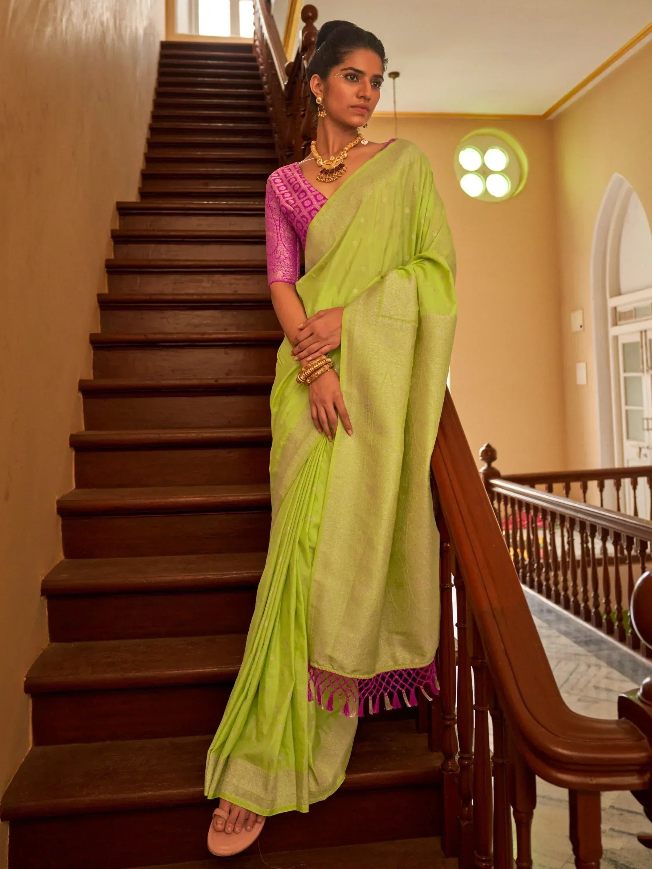 Woman in vibrant lime green saree with pink blouse, traditional Indian ethnic wear, standing on wooden staircase