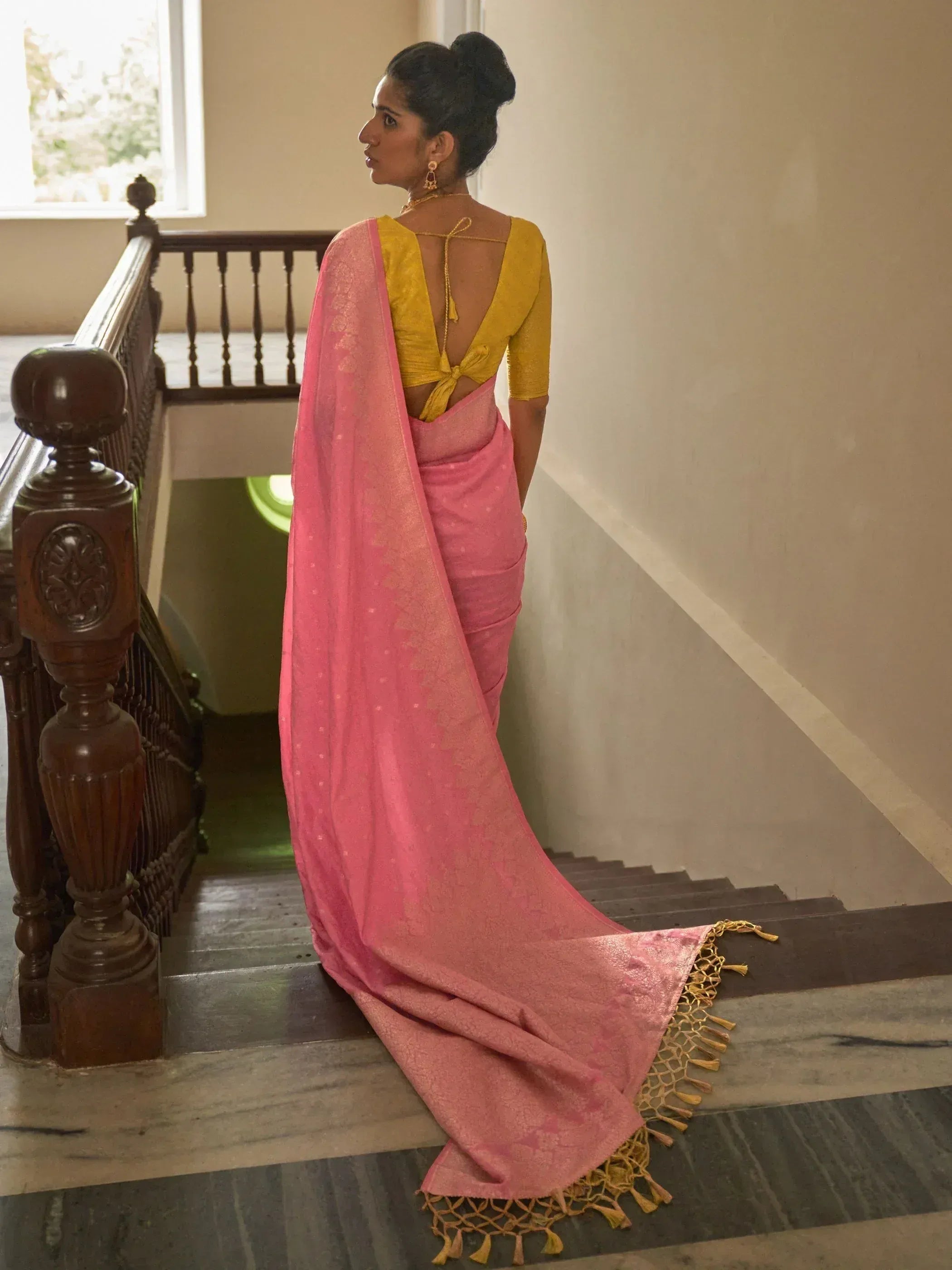 Pink saree with gold tassels and yellow backless blouse, styled on staircase for ethnic wear