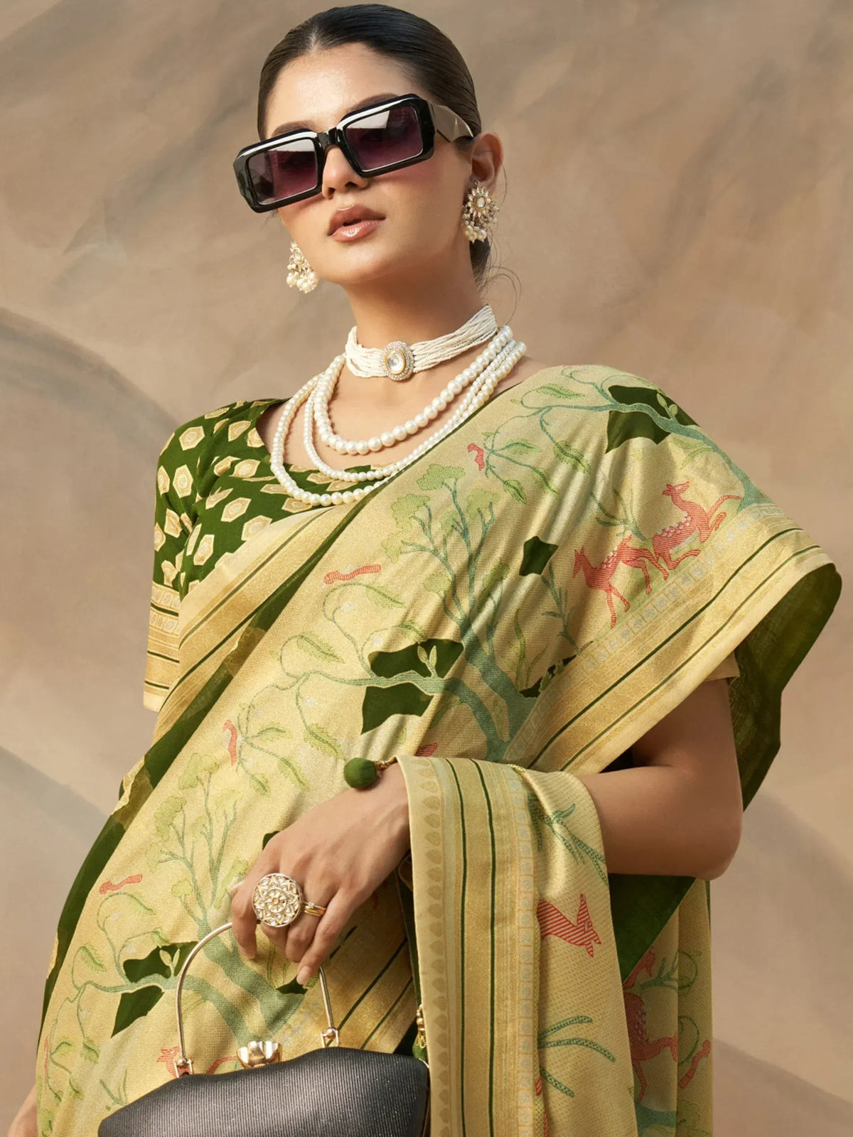 Woman in designer saree with deer print, pearl jewelry, and sunglasses, styled for ethnic fashion.