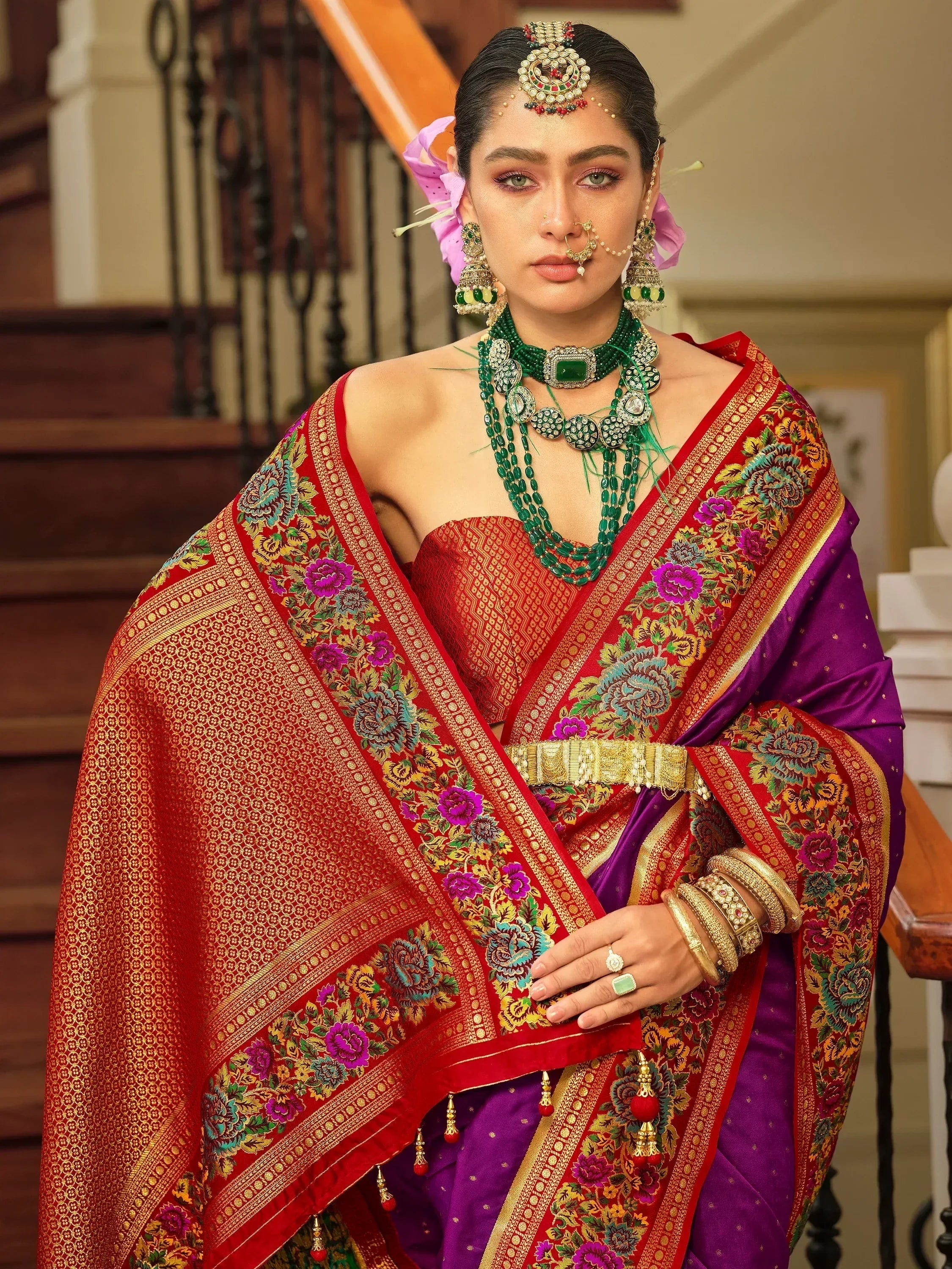 Woman in vibrant red and purple floral saree with gold embroidery, traditional Indian jewelry, and temple-style headpiece