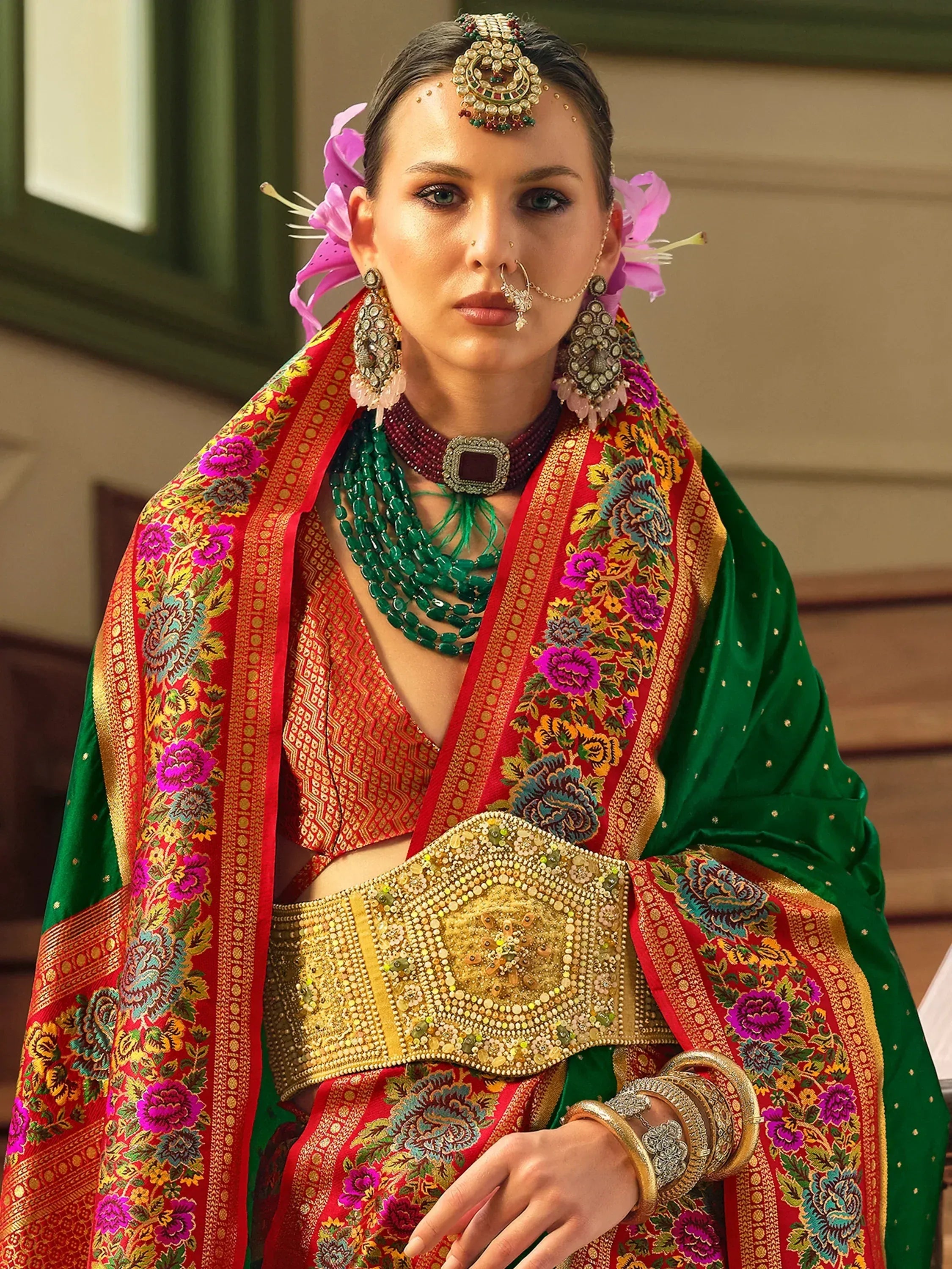 Indian bride in red and green embroidered lehenga choli with floral dupatta, traditional jewelry, and nose ring