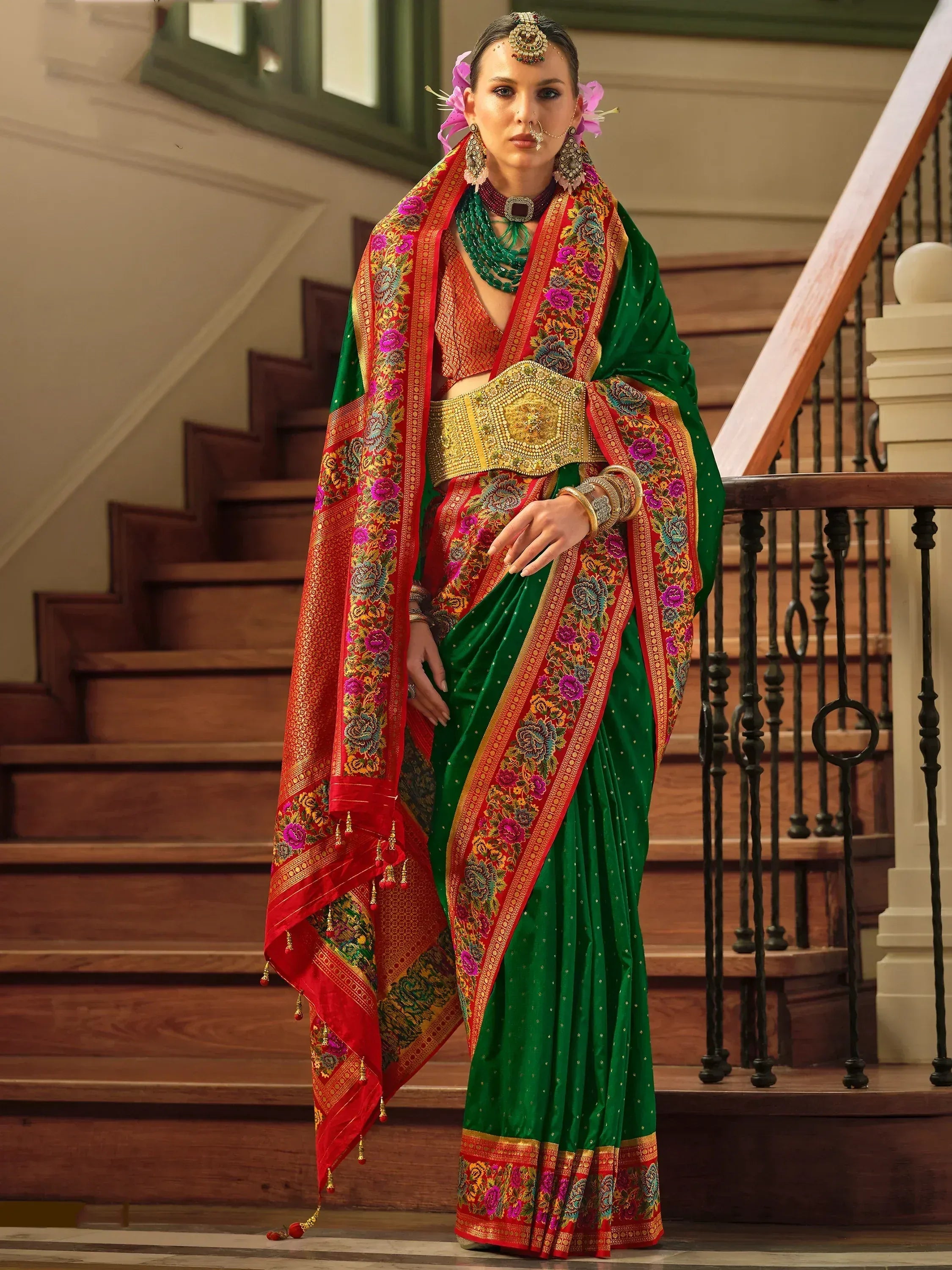 Green and red embroidered saree with floral border, gold belt, and traditional Indian jewelry for festive occasions