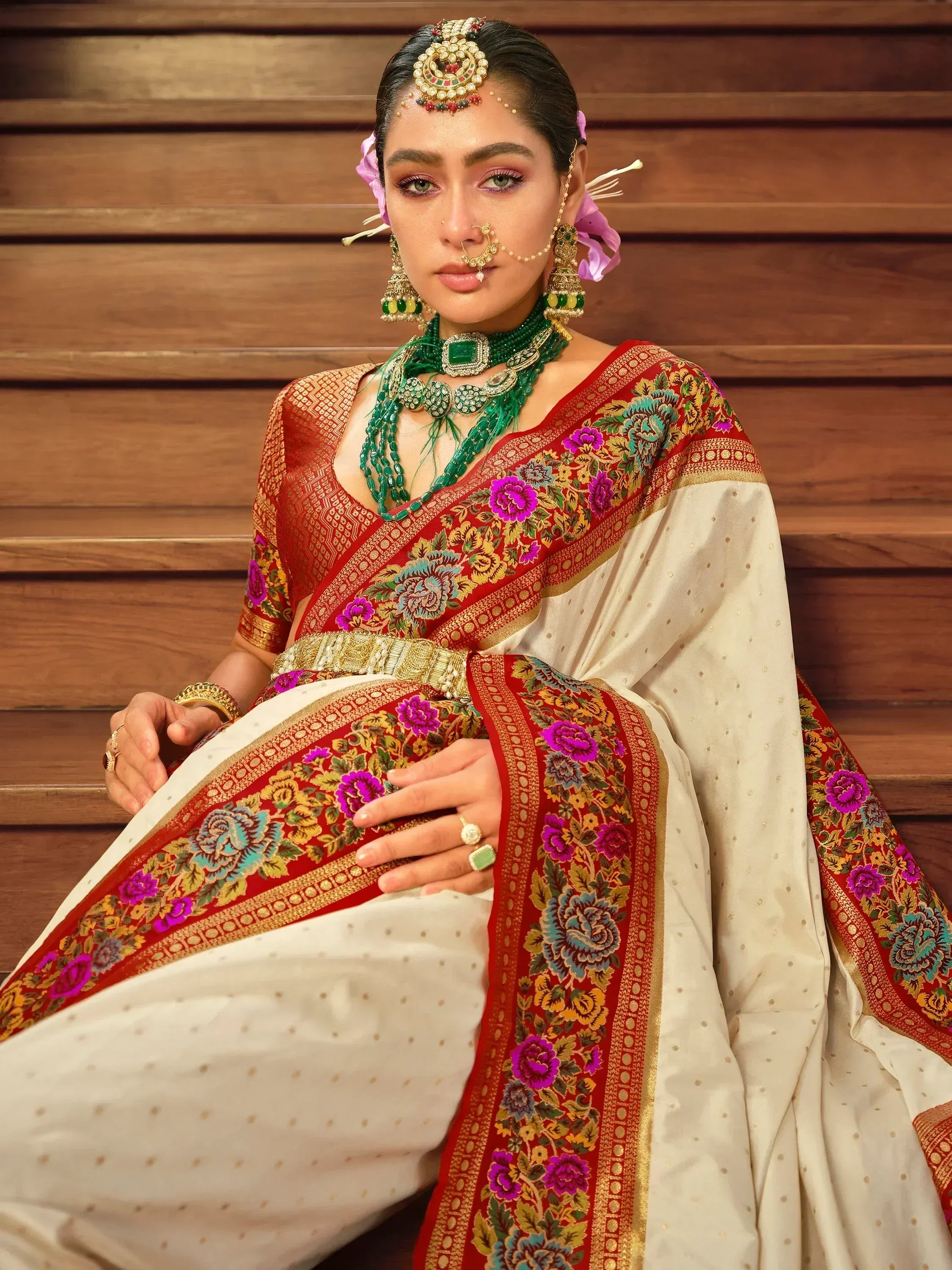 Woman in elegant white saree with red floral border, green jewelry, and traditional Indian bridal makeup