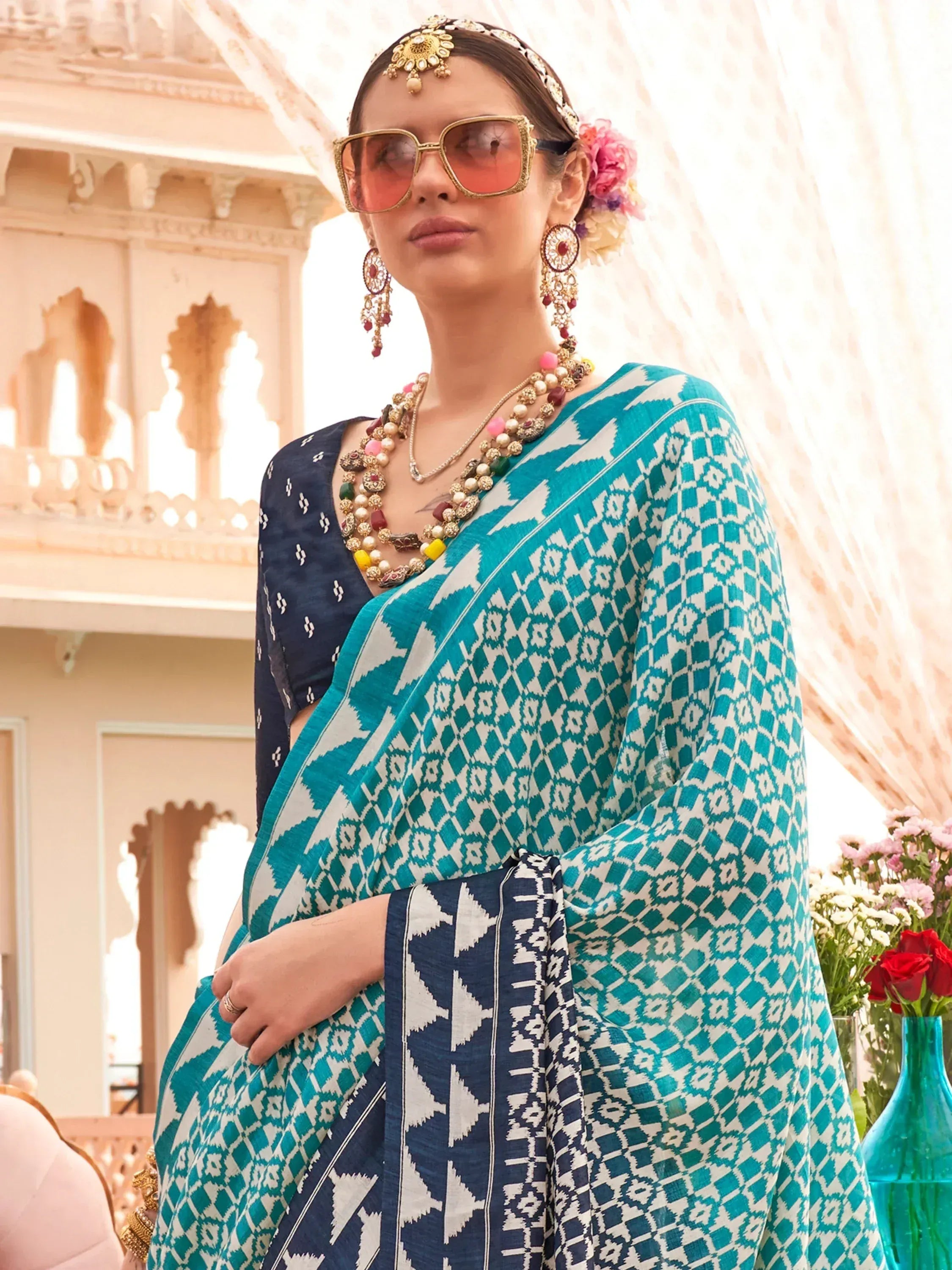 Woman in teal and navy ikat saree with ethnic jewelry and sunglasses, styled for Indian festive wear