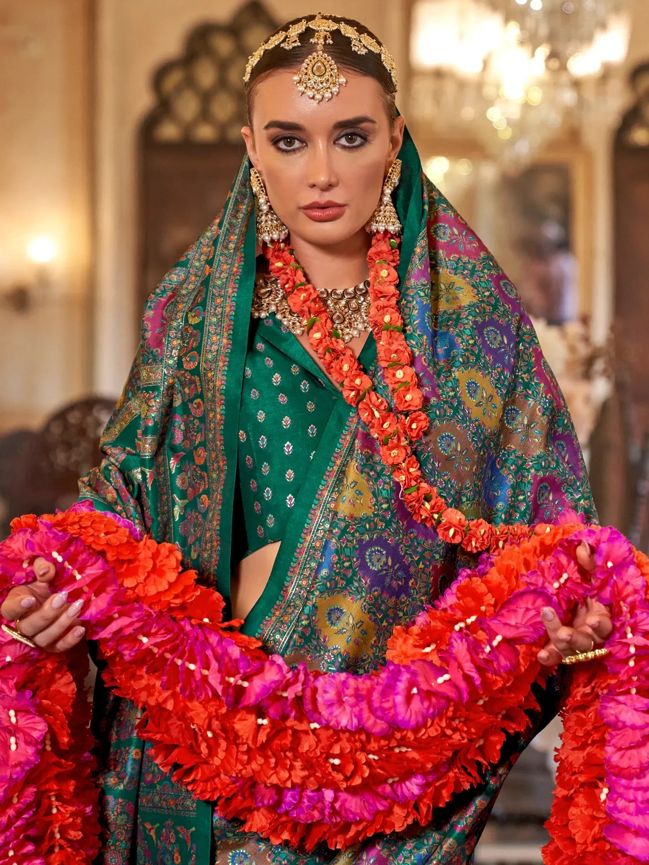 Elegant green ethnic saree with floral print, gold jewelry, and vibrant flower garlands for festive occasions.