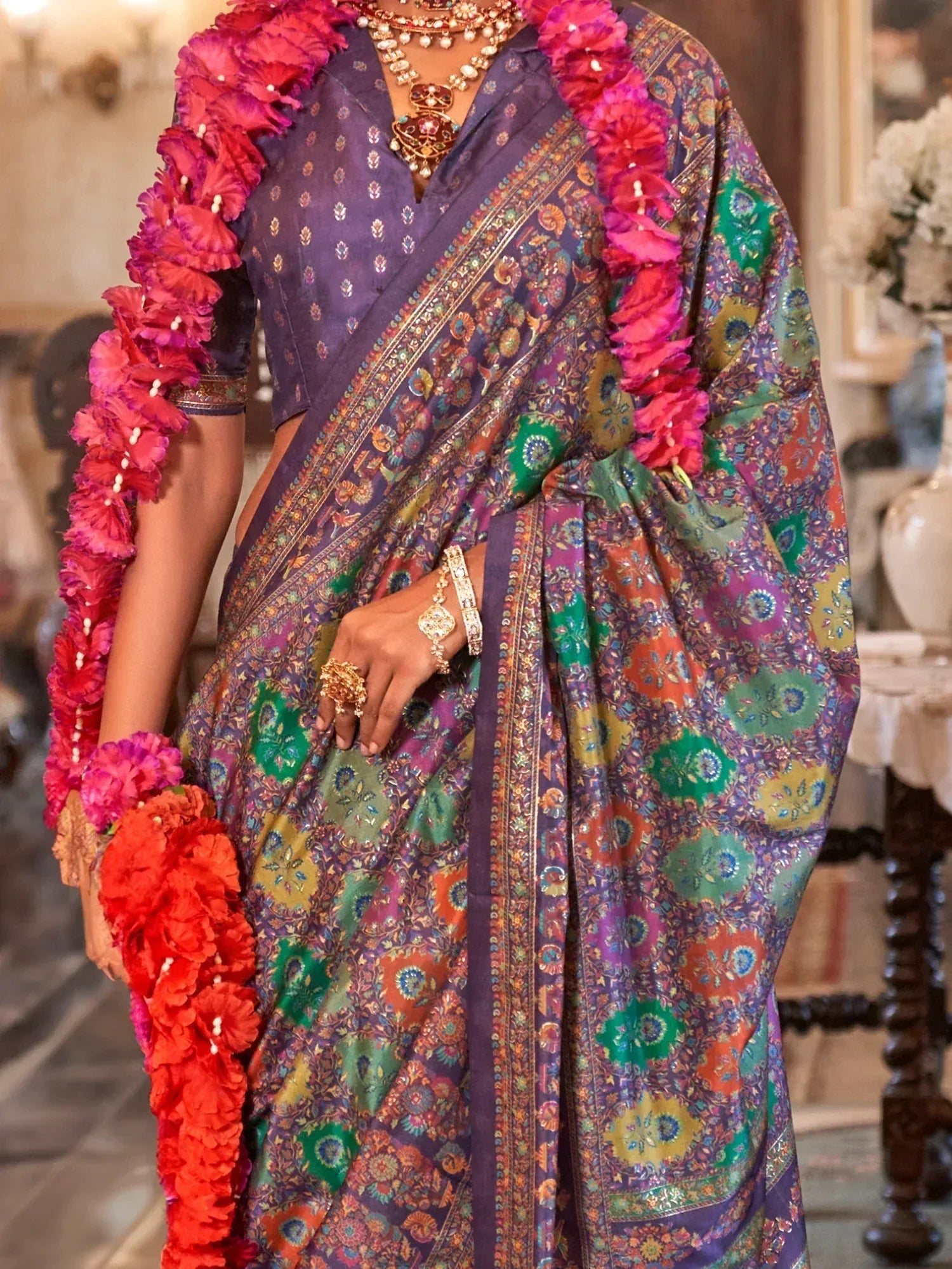 Purple floral saree with vibrant border, paired with gold jewelry and pink flower garland, perfect for Indian ethnic occasions