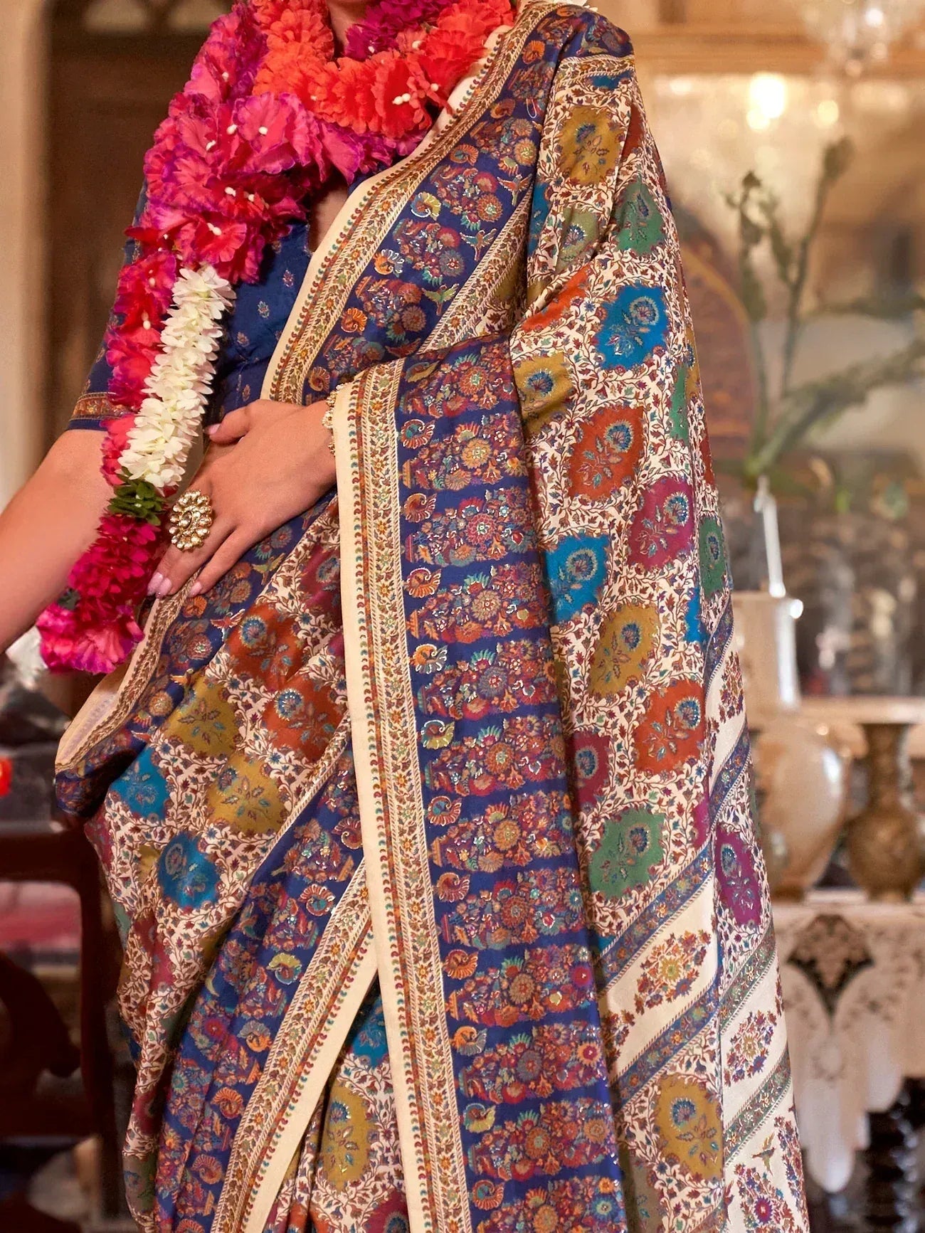 Vibrant floral printed saree with intricate borders, paired with a colorful flower garland.