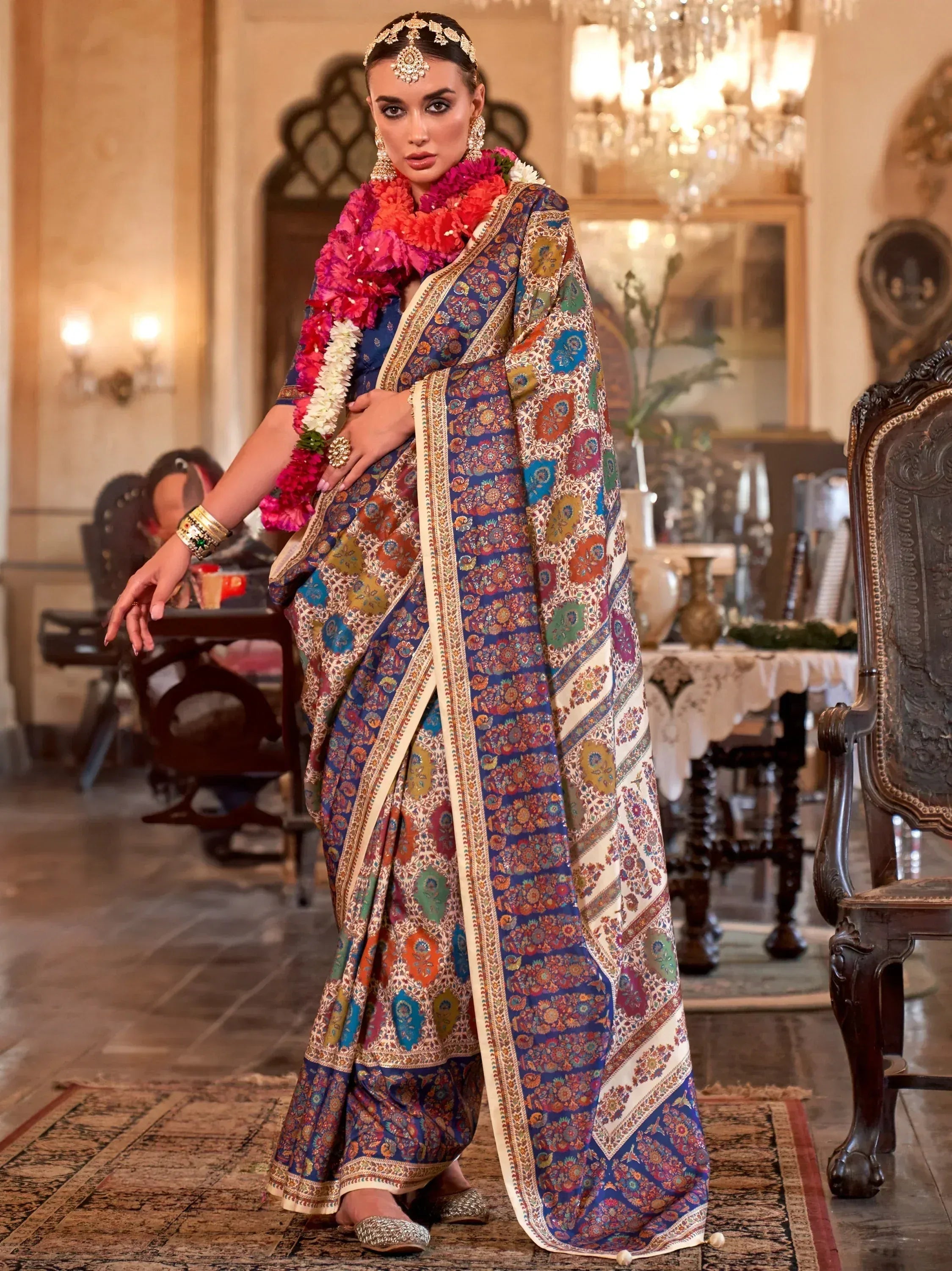 Elegant woman in vibrant floral print saree with gold border, traditional jewelry, and floral garland, perfect for Indian ethnic wear occasions.