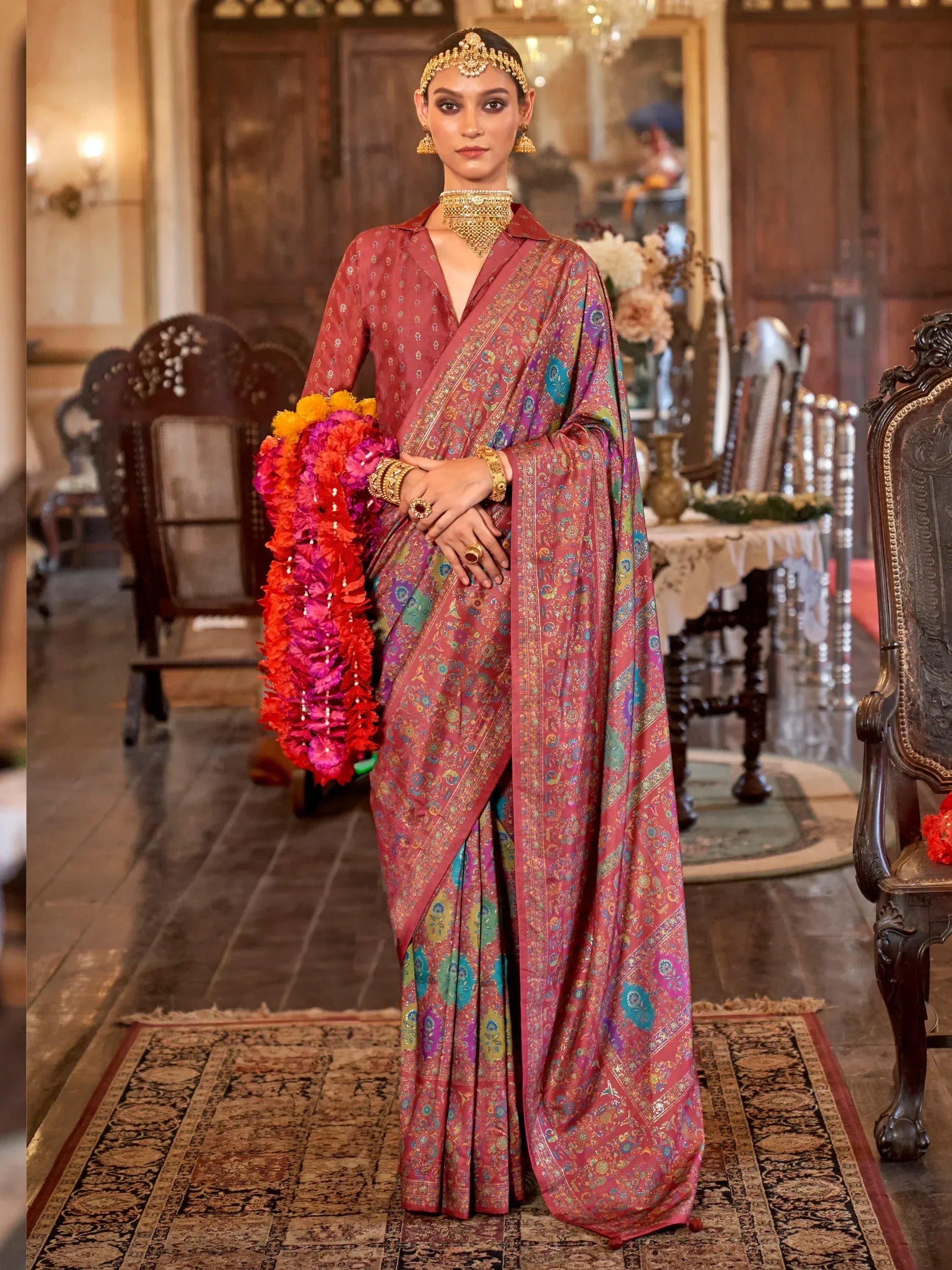 Woman in elegant maroon floral saree with gold jewelry, holding colorful garland, traditional Indian ethnic wear