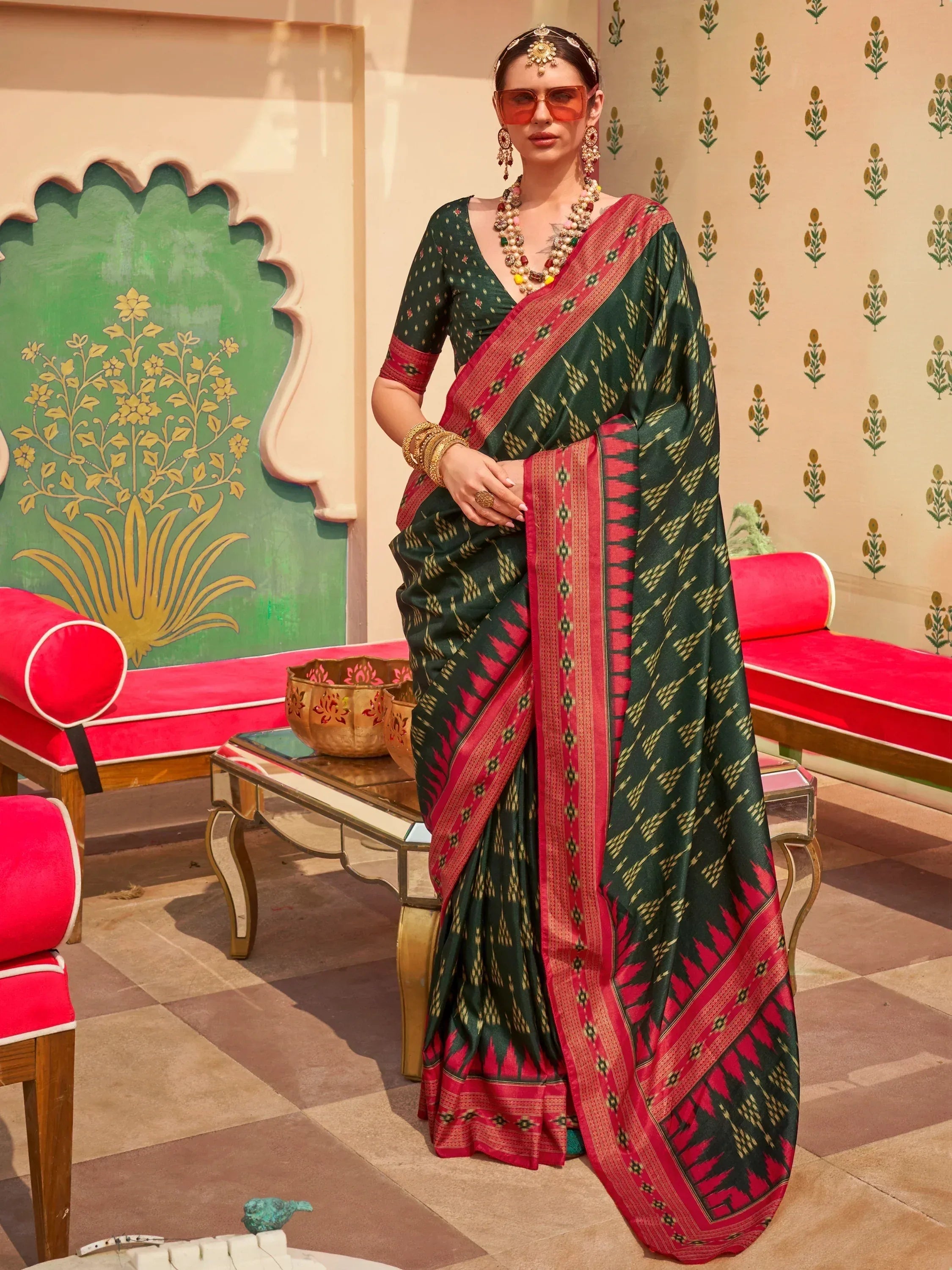 Woman in green and red ethnic saree with gold ikat print, traditional jewelry, and sunglasses