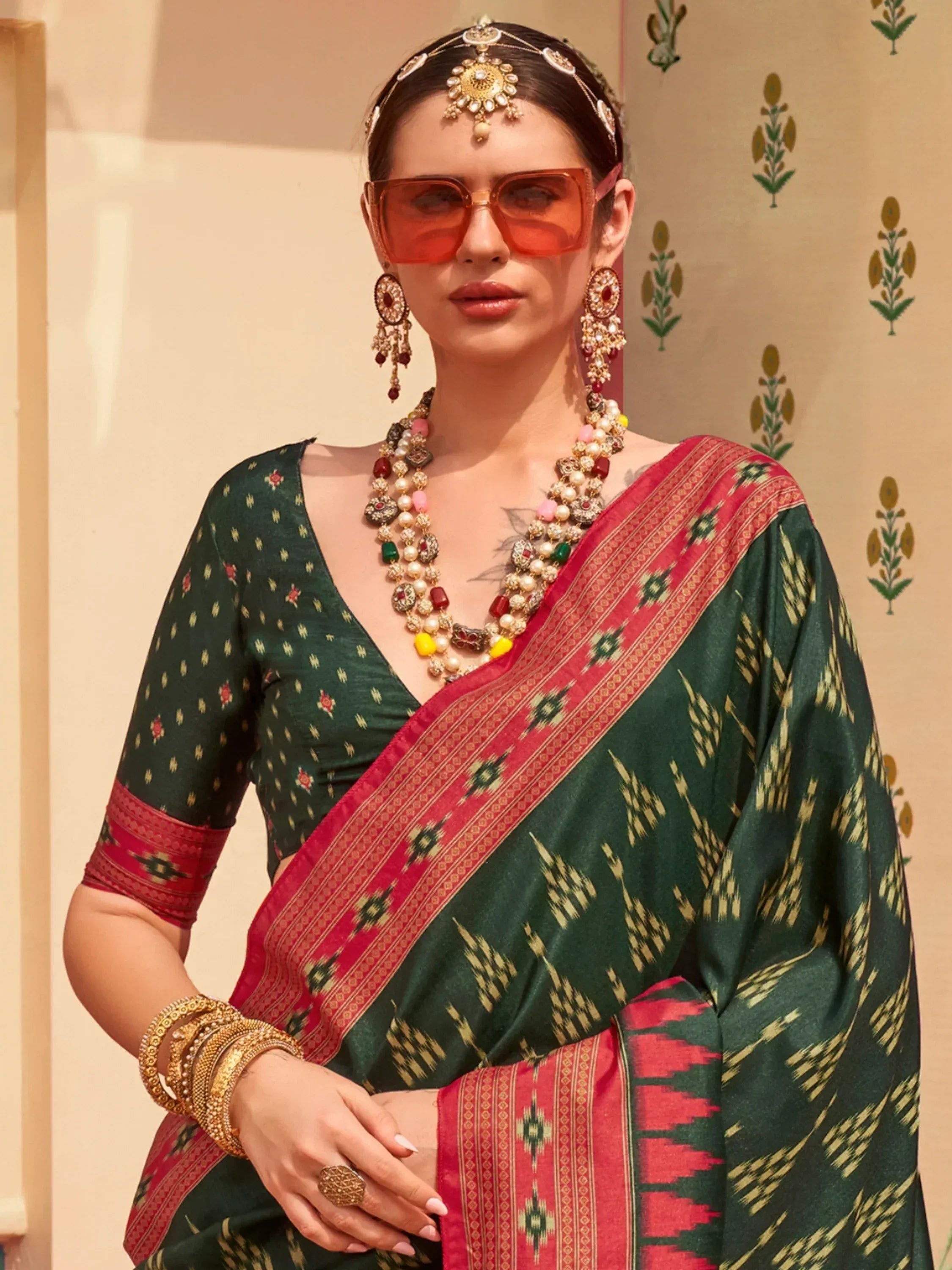 Woman in green and red ethnic saree with traditional jewelry and sunglasses, Indian designer wear