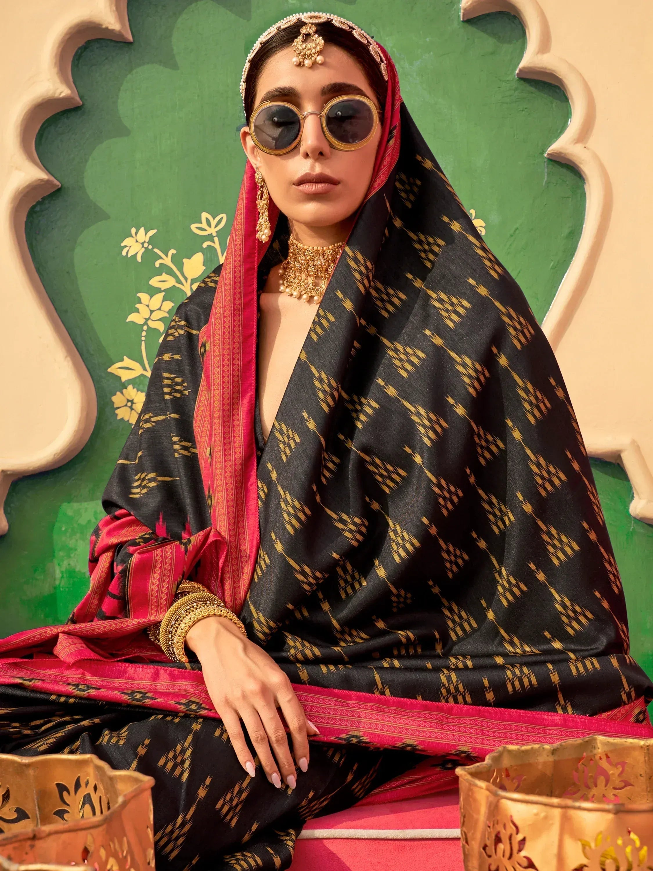 Black and gold ikat saree with pink border, styled with traditional jewelry and sunglasses for ethnic wear.
