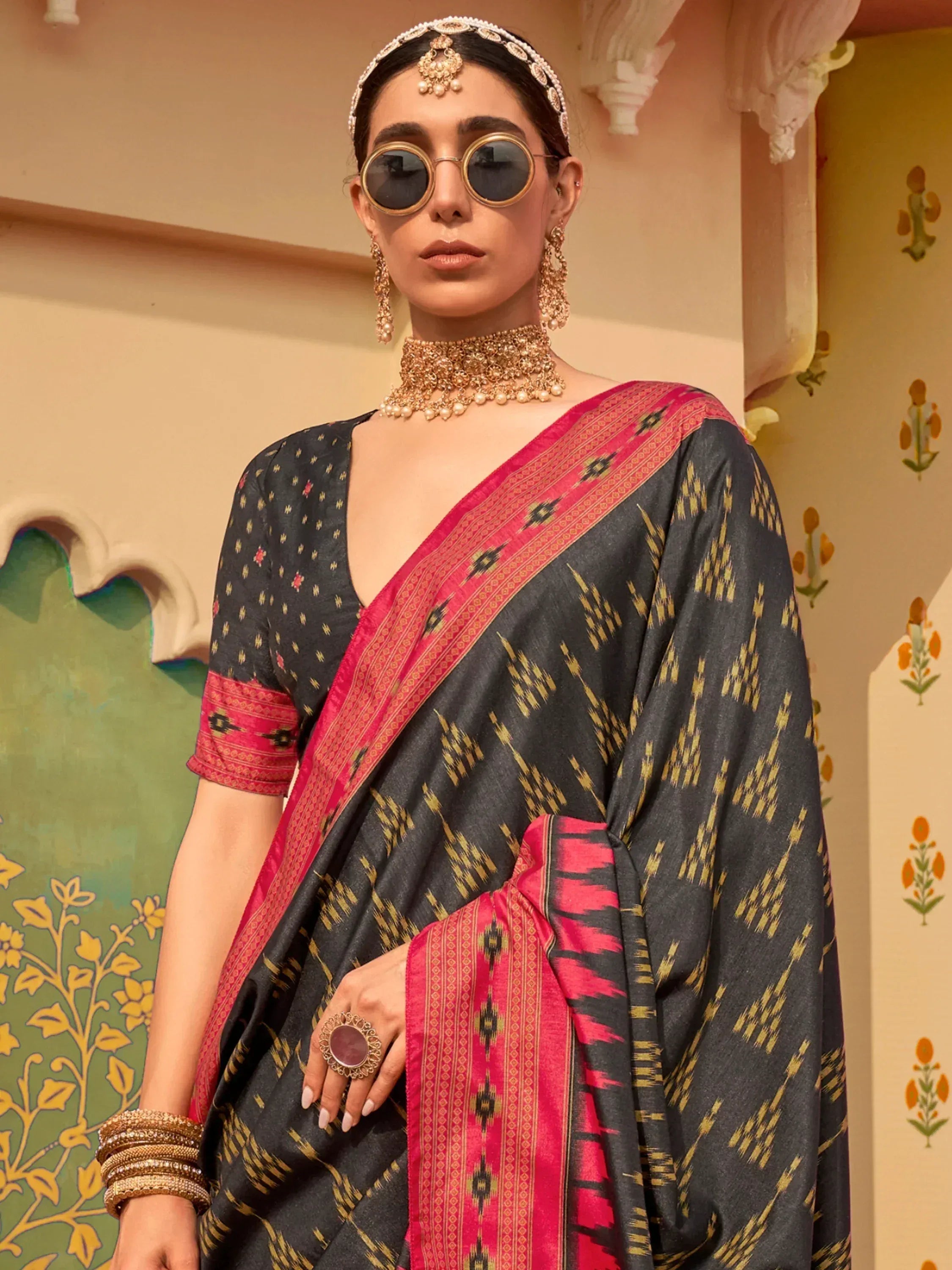 Stylish black and pink ikat saree with gold patterns, paired with traditional jewelry and sunglasses