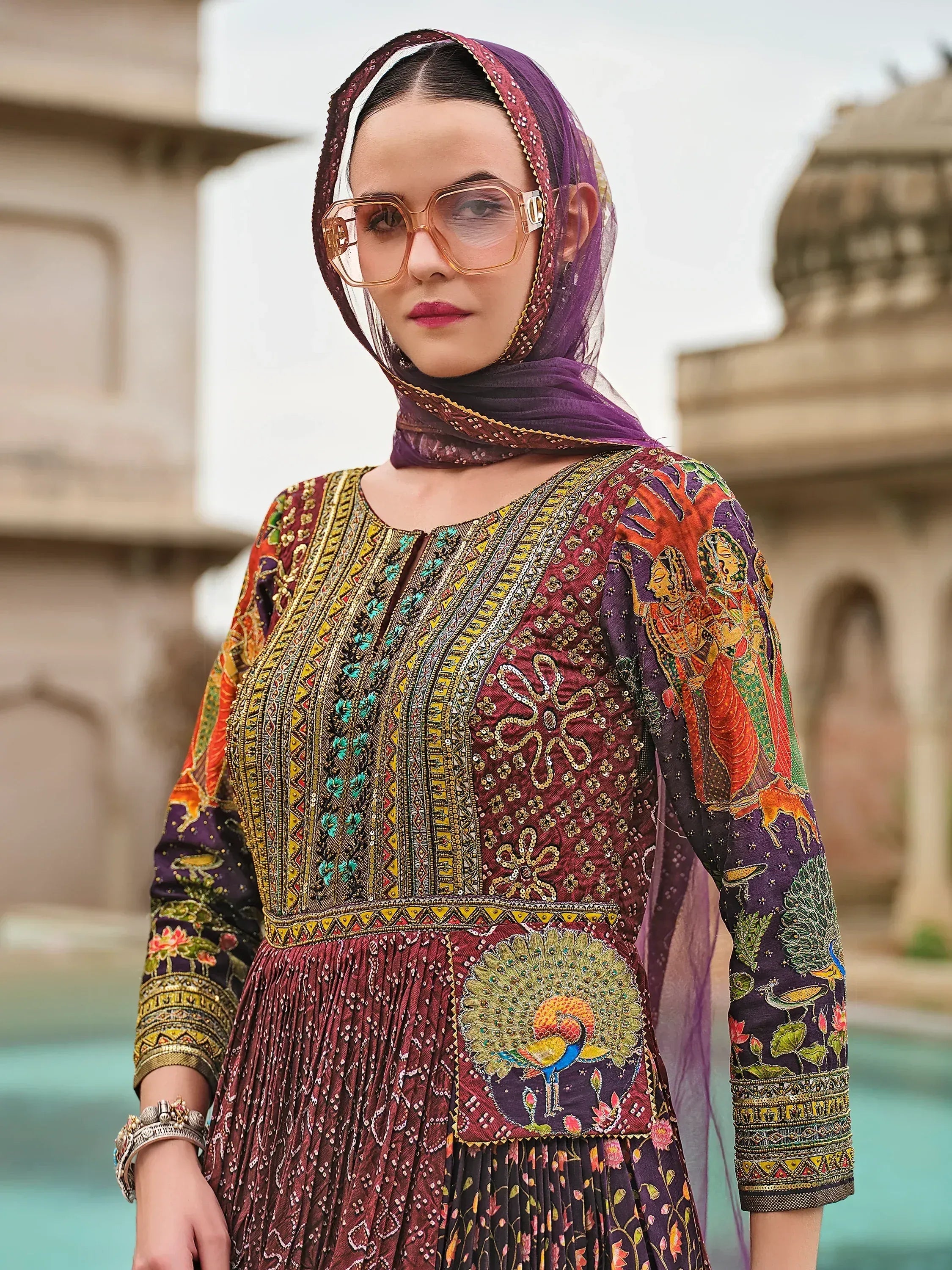 Woman in colorful embroidered ethnic gown with peacock design, purple dupatta, and statement sunglasses