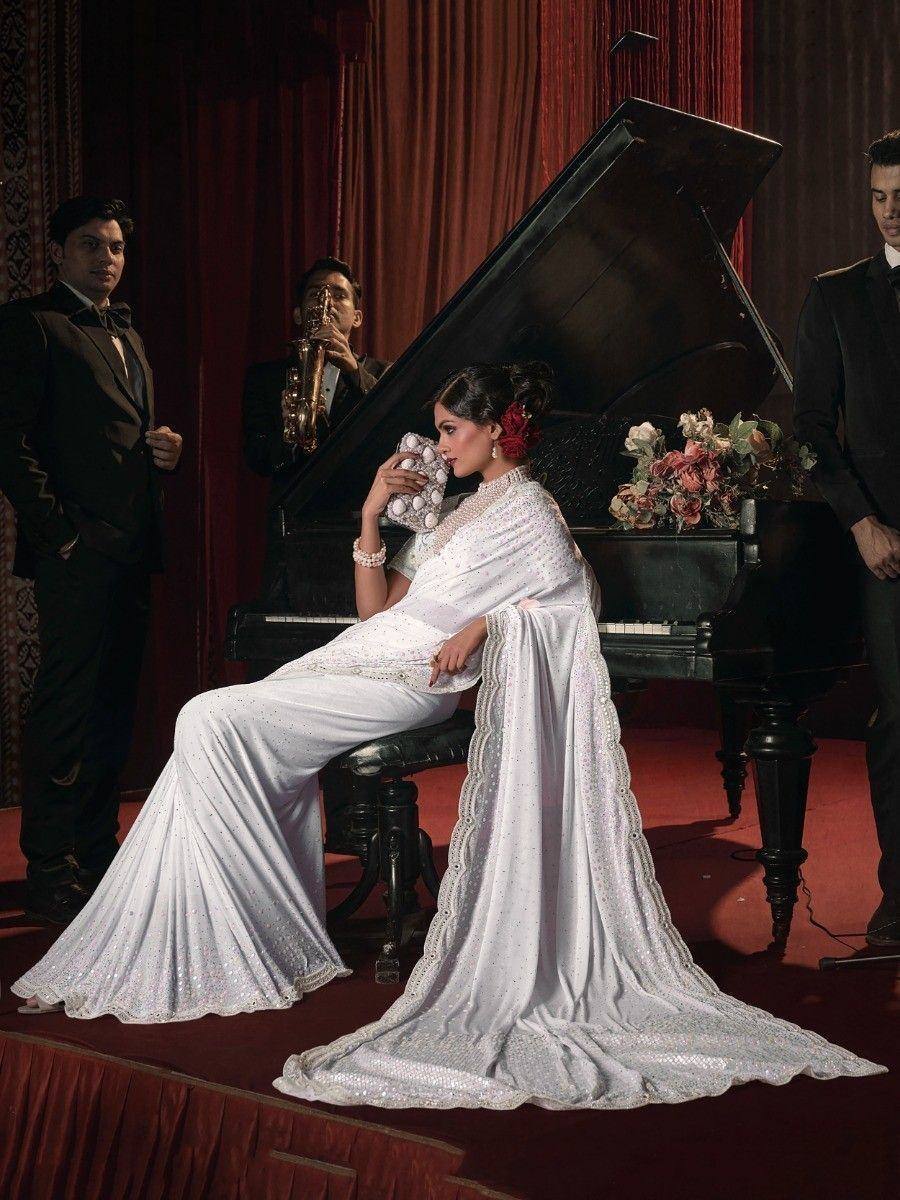 Elegant white ethnic gown with sequin detailing, worn by woman seated beside grand piano in luxury setting