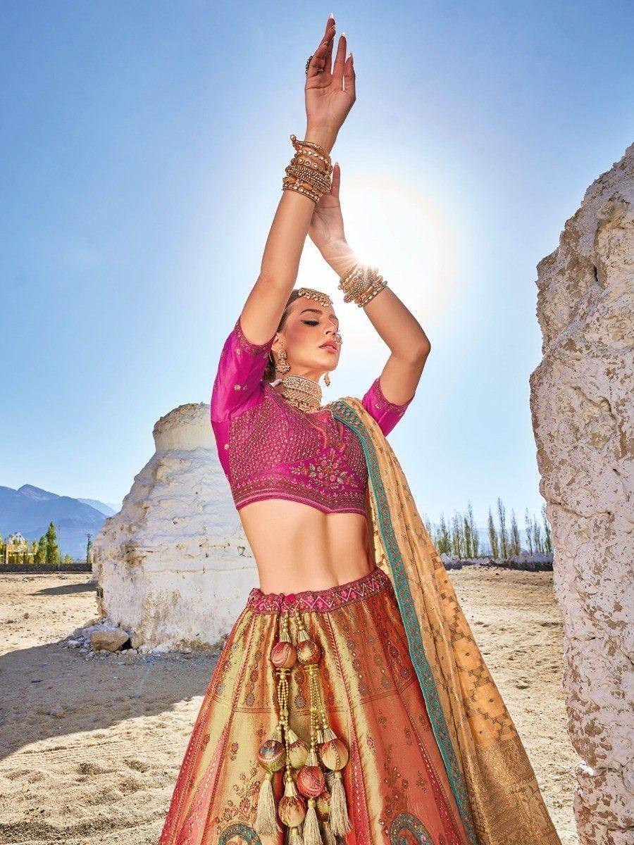Woman in pink embroidered lehenga choli with gold dupatta, posing outdoors under bright sun
