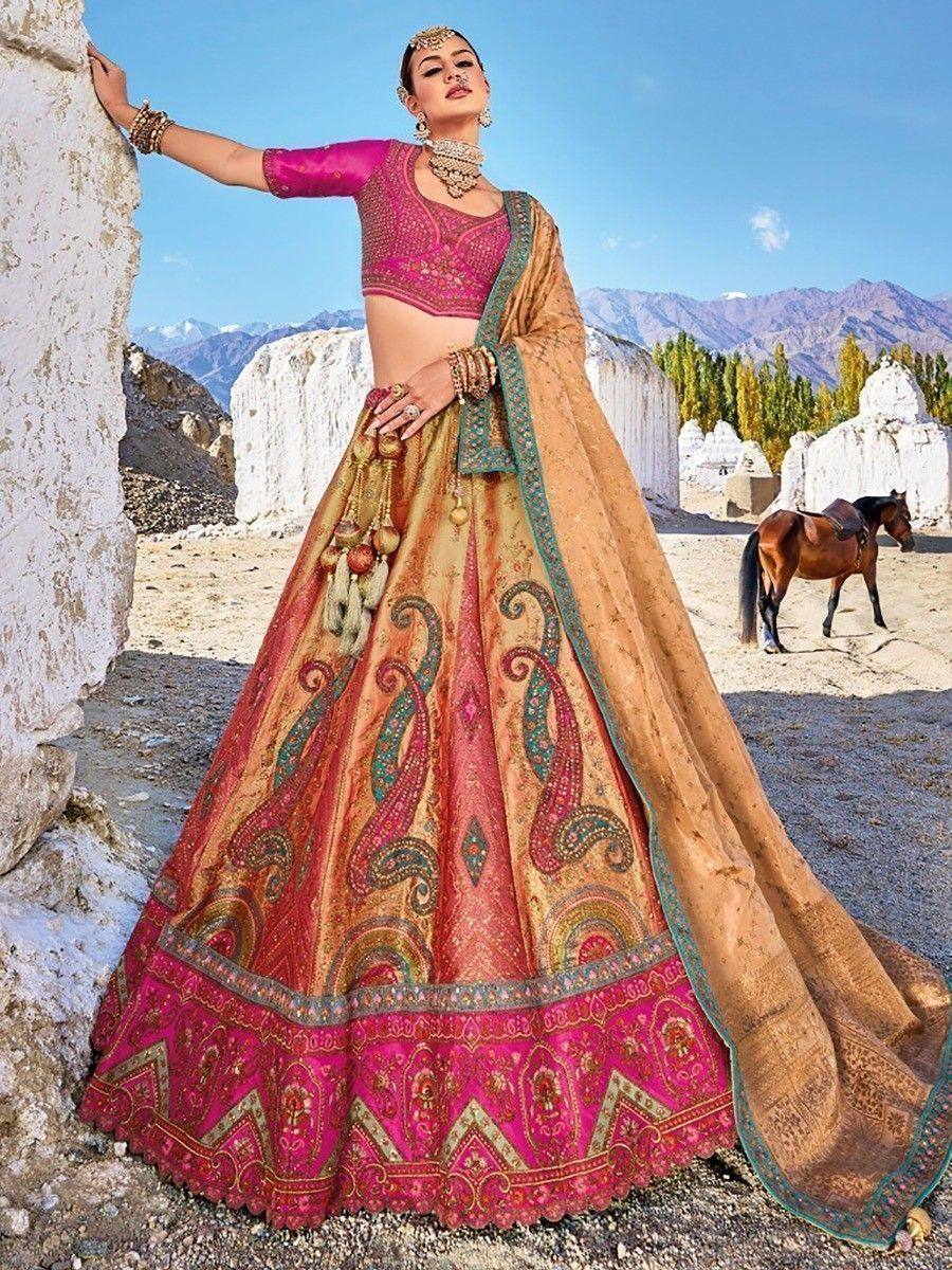Woman in vibrant pink and gold designer lehenga choli with paisley print, set against mountainous desert backdrop