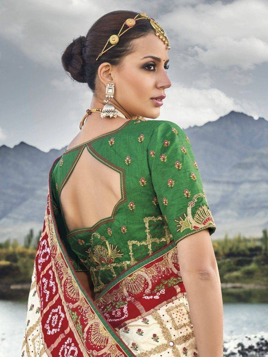 Green embroidered saree blouse with back cutout, paired with red and cream saree, mountain backdrop
