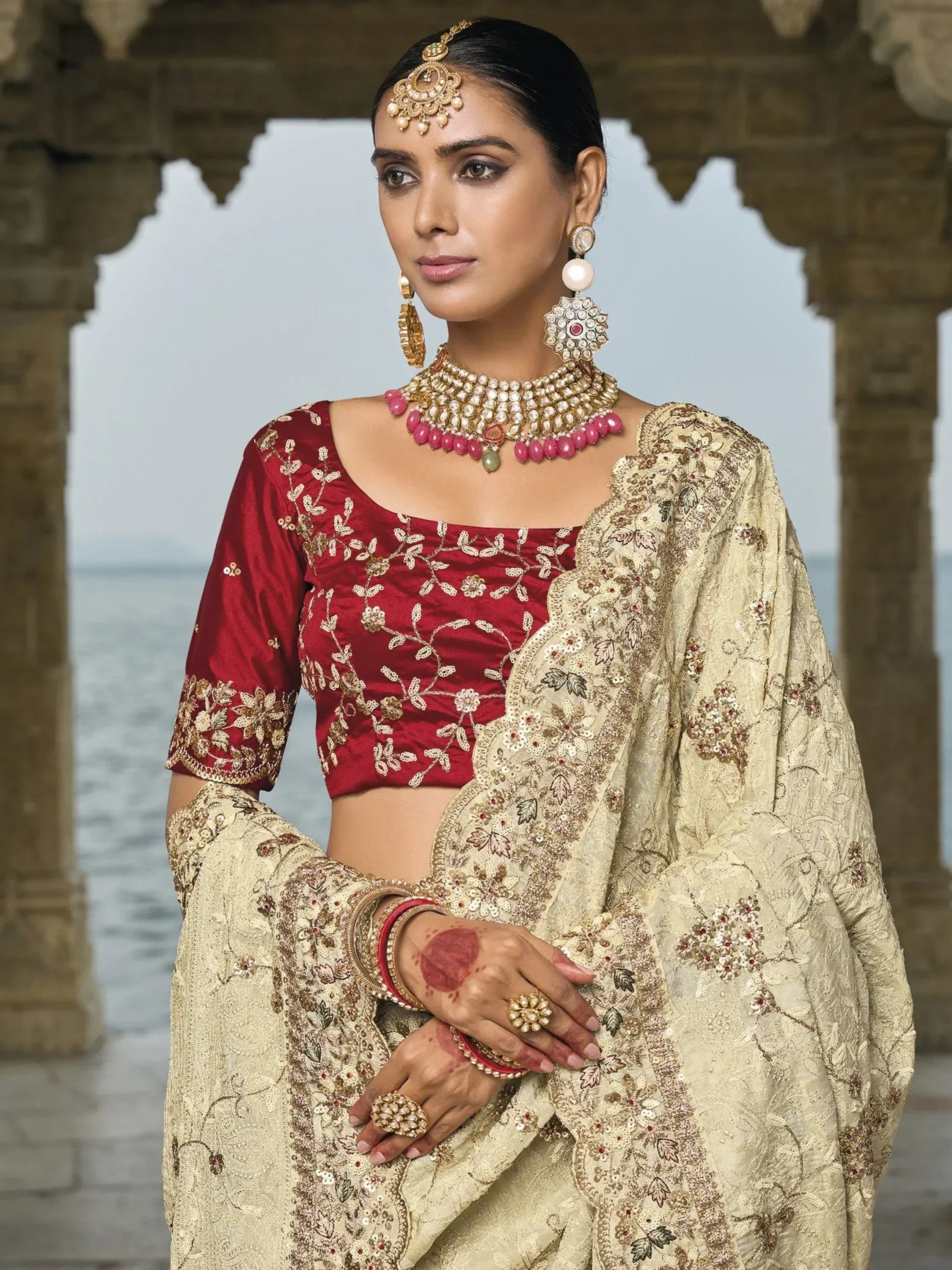 Woman in red embroidered blouse and gold floral lehenga with traditional Indian jewelry, perfect for weddings or festive occasions.