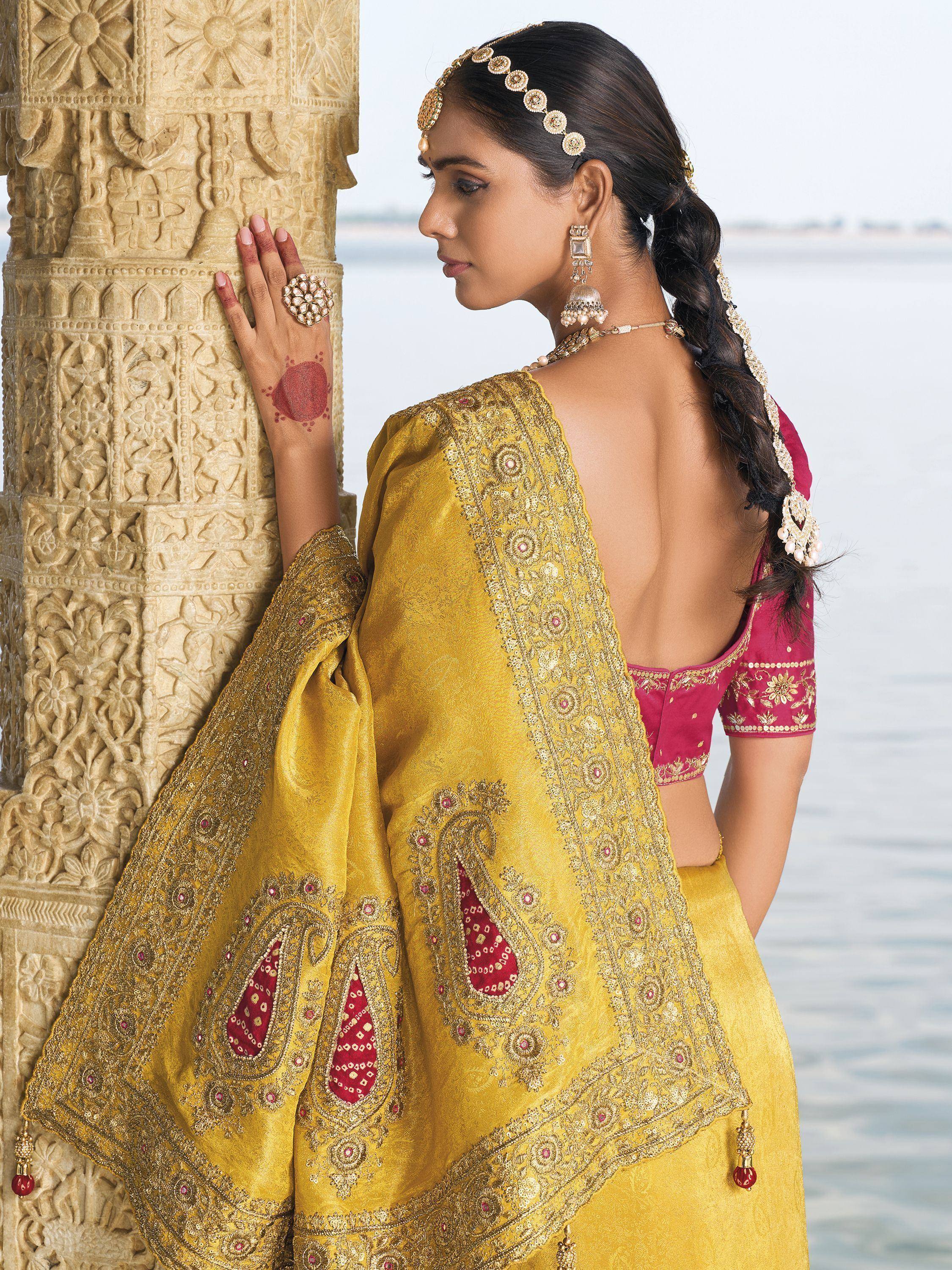 Yellow embroidered lehenga choli with pink blouse, traditional Indian ethnic wear, gold jewelry, carved pillar backdrop
