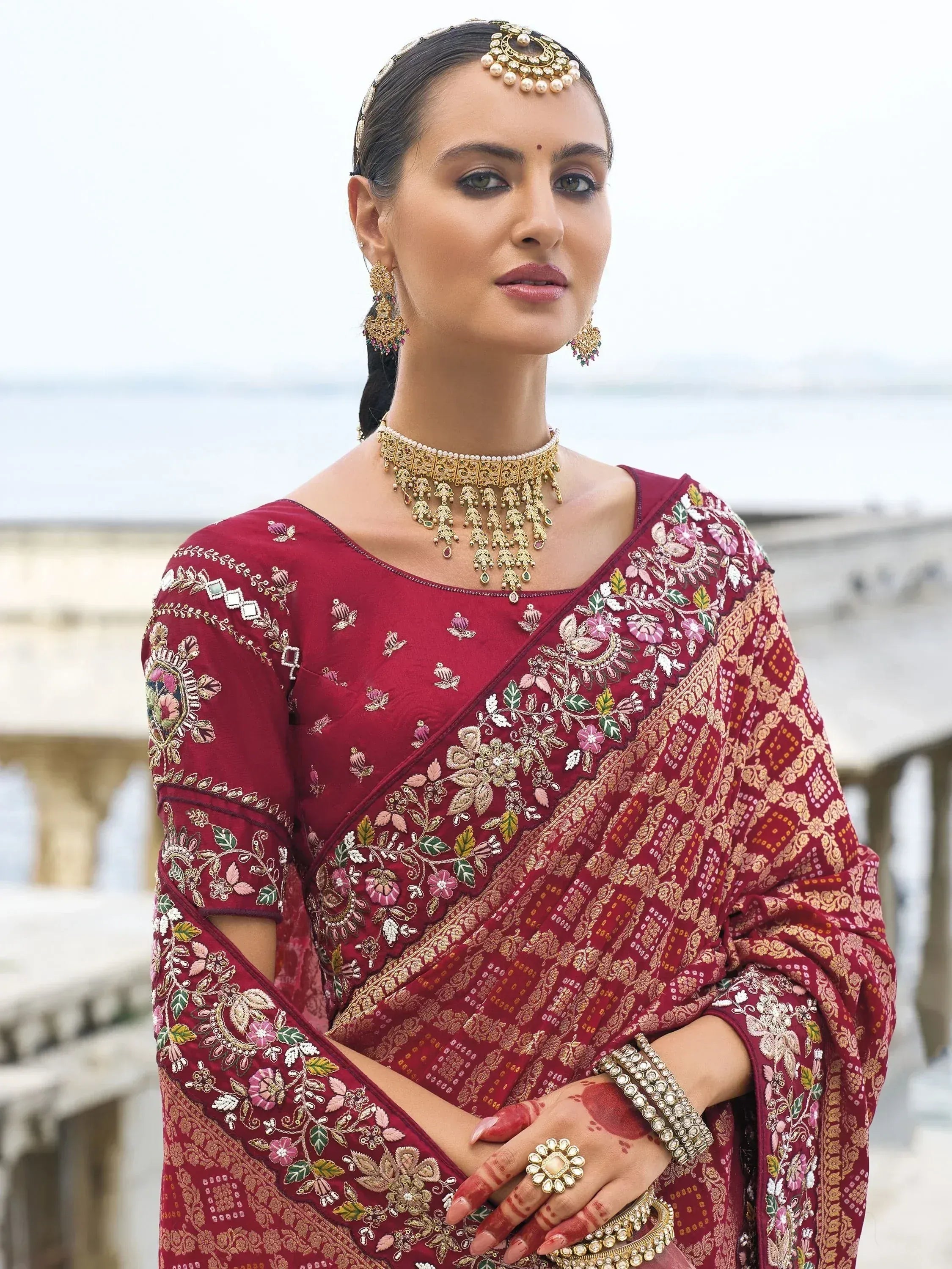 Maroon embroidered saree with floral designs, gold jewelry, and traditional Indian bridal look