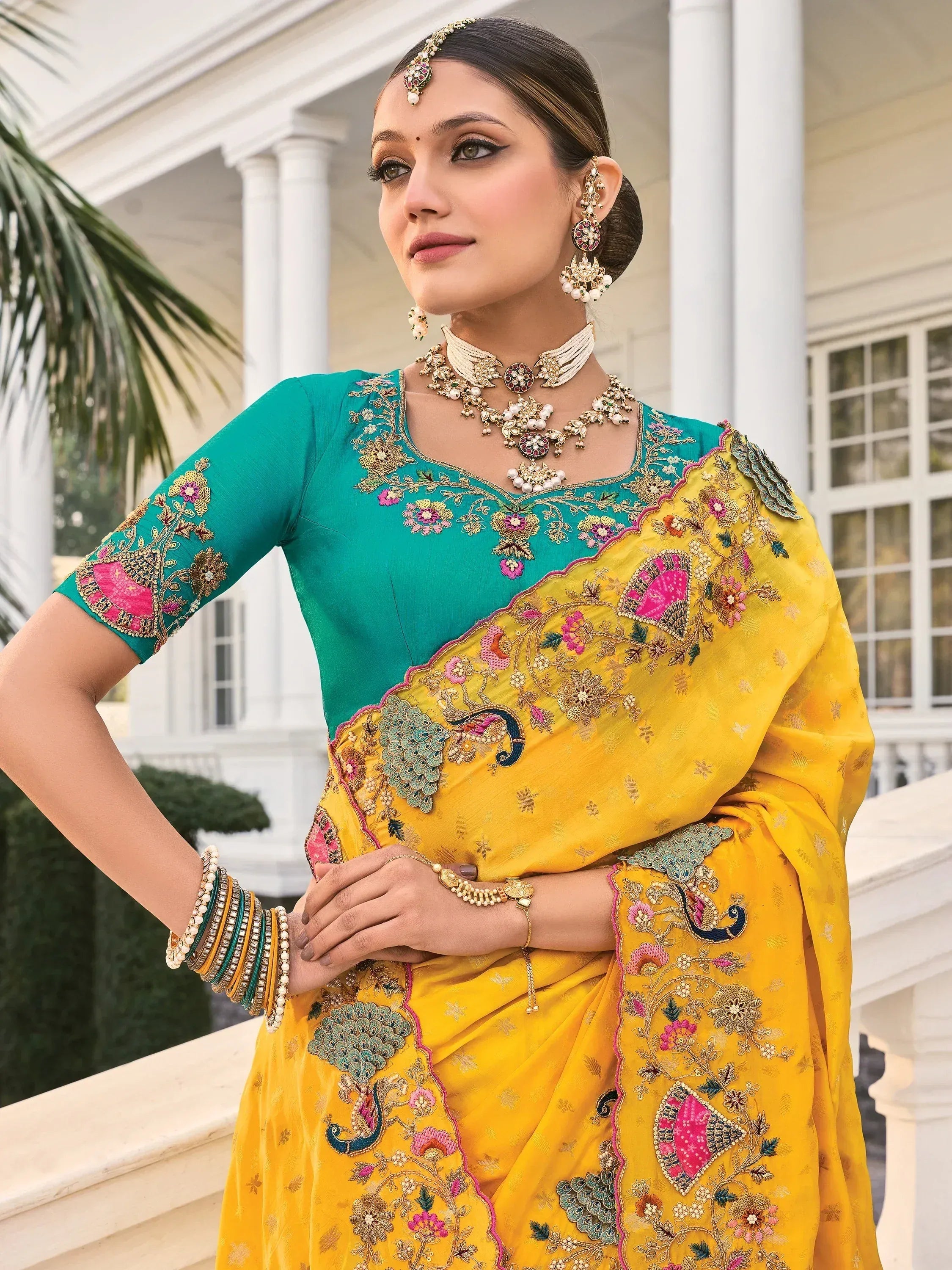 Elegant yellow and teal embroidered saree with floral and peacock motifs, paired with traditional jewelry.