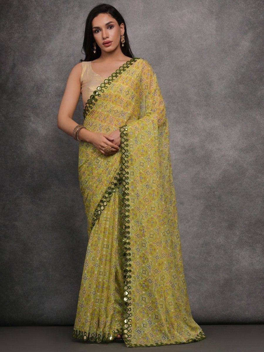 Yellow printed saree with green mirror work border, paired with sleeveless blouse for ethnic wear