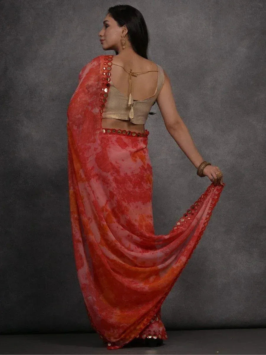 Woman in vibrant red-orange tie-dye saree with mirror work, paired with gold blouse, showcasing ethnic Indian wear.