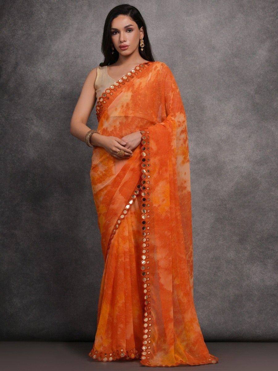 Orange tie-dye saree with mirror work, styled with gold blouse and jewelry for ethnic wear