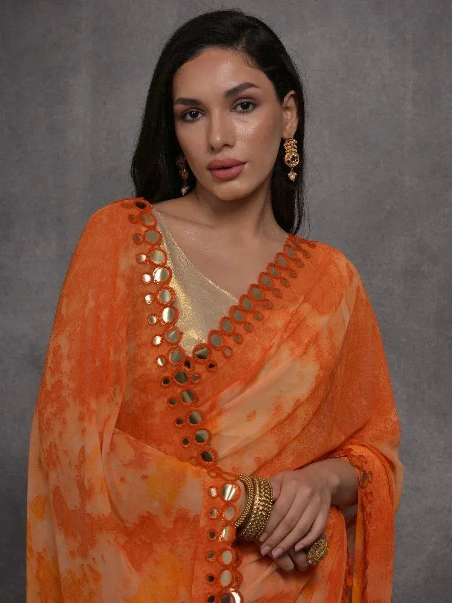 Orange ethnic saree with mirror work and gold blouse, styled with jhumka earrings and bangles