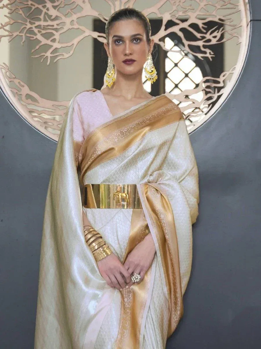 Elegant white and gold saree with intricate embroidery and golden belt, styled with statement jewelry.