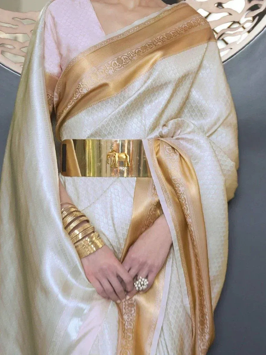 Elegant cream saree with golden border, paired with gold belt and bangles, showcasing Indian ethnic wear.