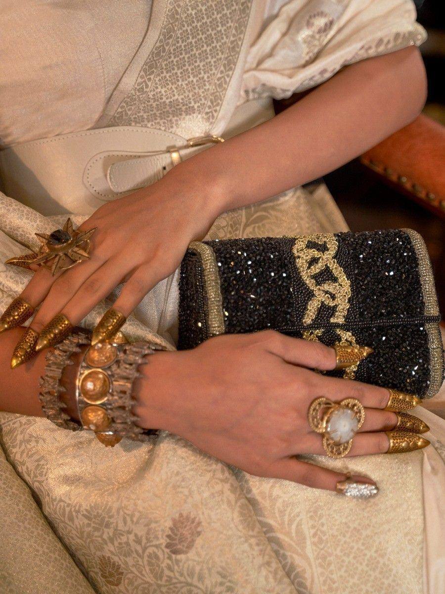 Elegant ethnic wear with gold jewelry, statement rings, and beaded clutch for festive occasions