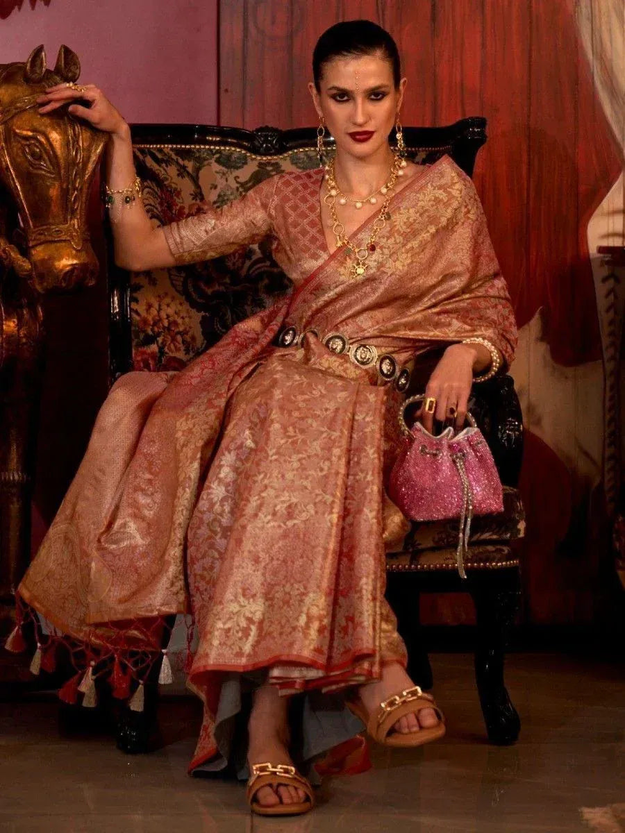 Woman in elegant pink and gold designer saree with traditional jewelry and pink handbag, seated on ornate chair