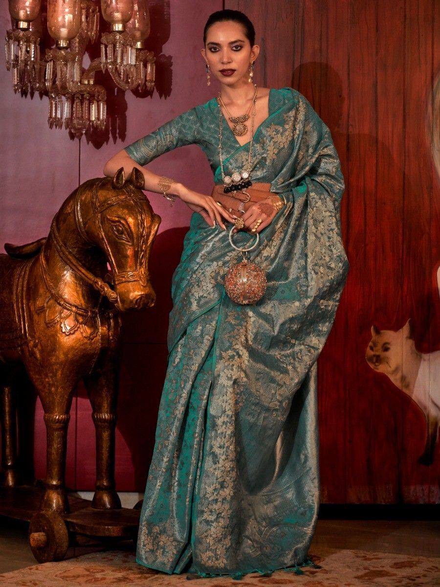 Teal designer saree with gold embroidery, styled with statement jewelry and a belt, perfect for ethnic occasions.