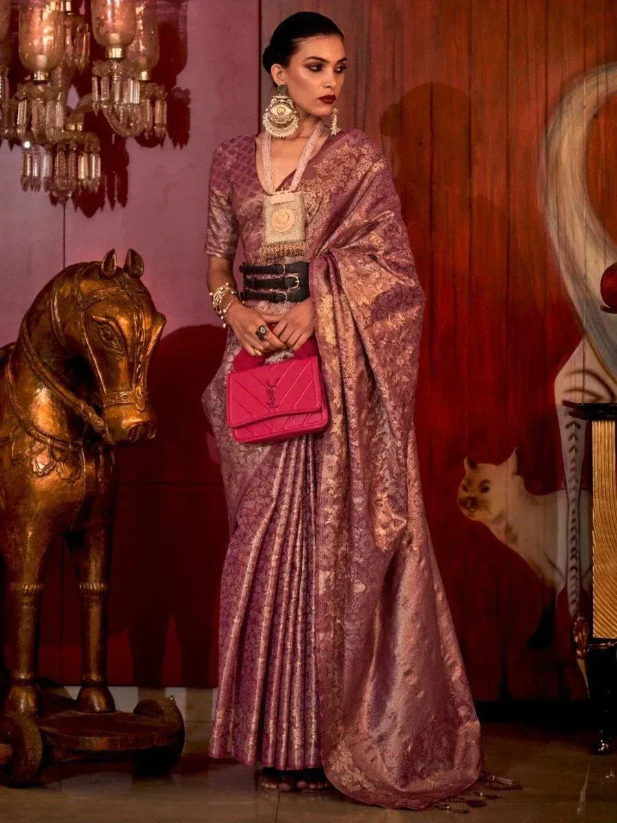 Woman in purple designer saree with gold embroidery, statement jewelry, and pink clutch, styled for ethnic occasions.