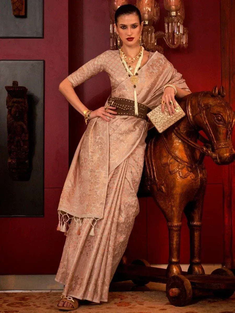 Elegant beige designer saree with gold embroidery, paired with statement jewelry and a studded belt, styled for festive occasions.