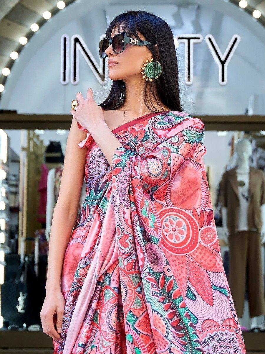 Woman in vibrant pink floral ethnic gown with one-shoulder design, styled with statement earrings and sunglasses.