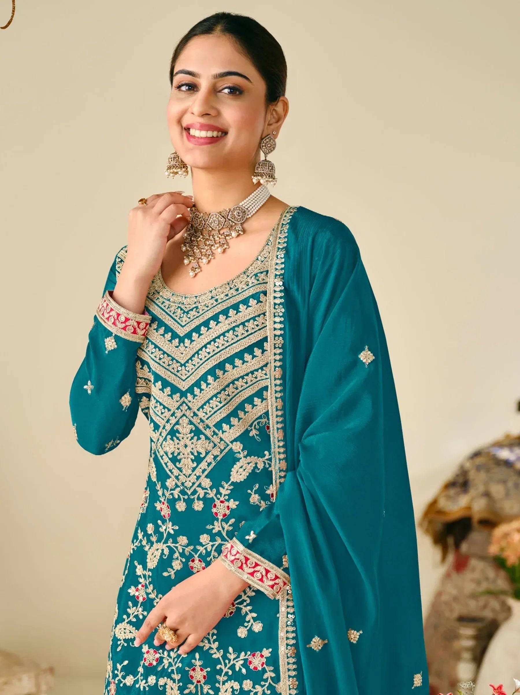Teal embroidered Indian ethnic gown with gold and red detailing, paired with traditional jewelry