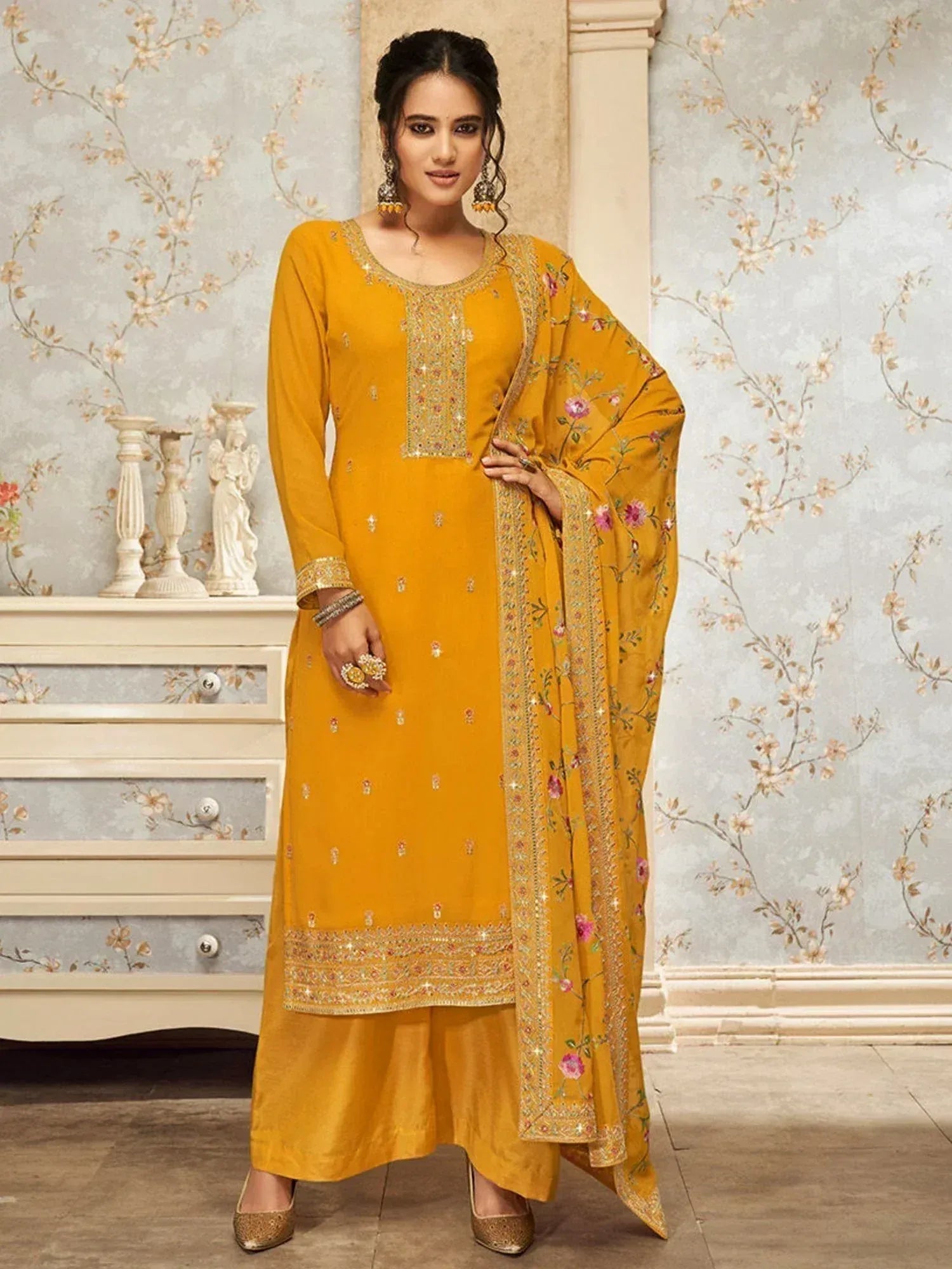 Woman wearing mustard yellow embroidered salwar kameez with dupatta, floral pattern background