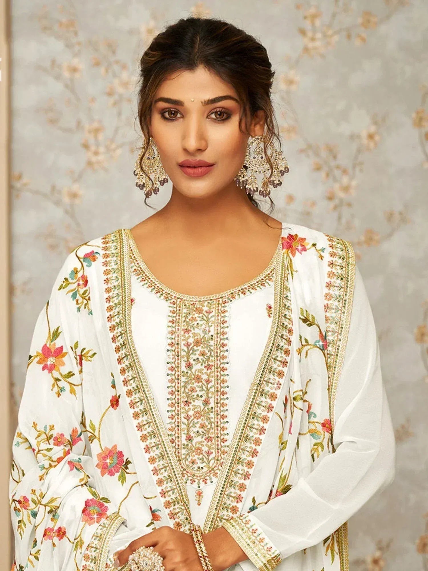 Woman wearing white embroidered salwar kameez with floral designs and statement earrings