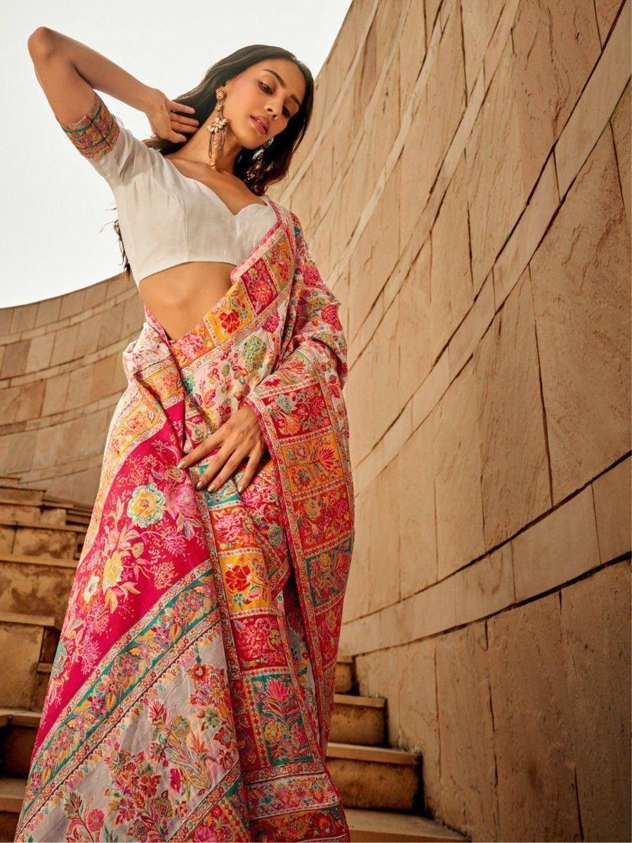 Woman in vibrant floral saree with white blouse, posing against stone steps