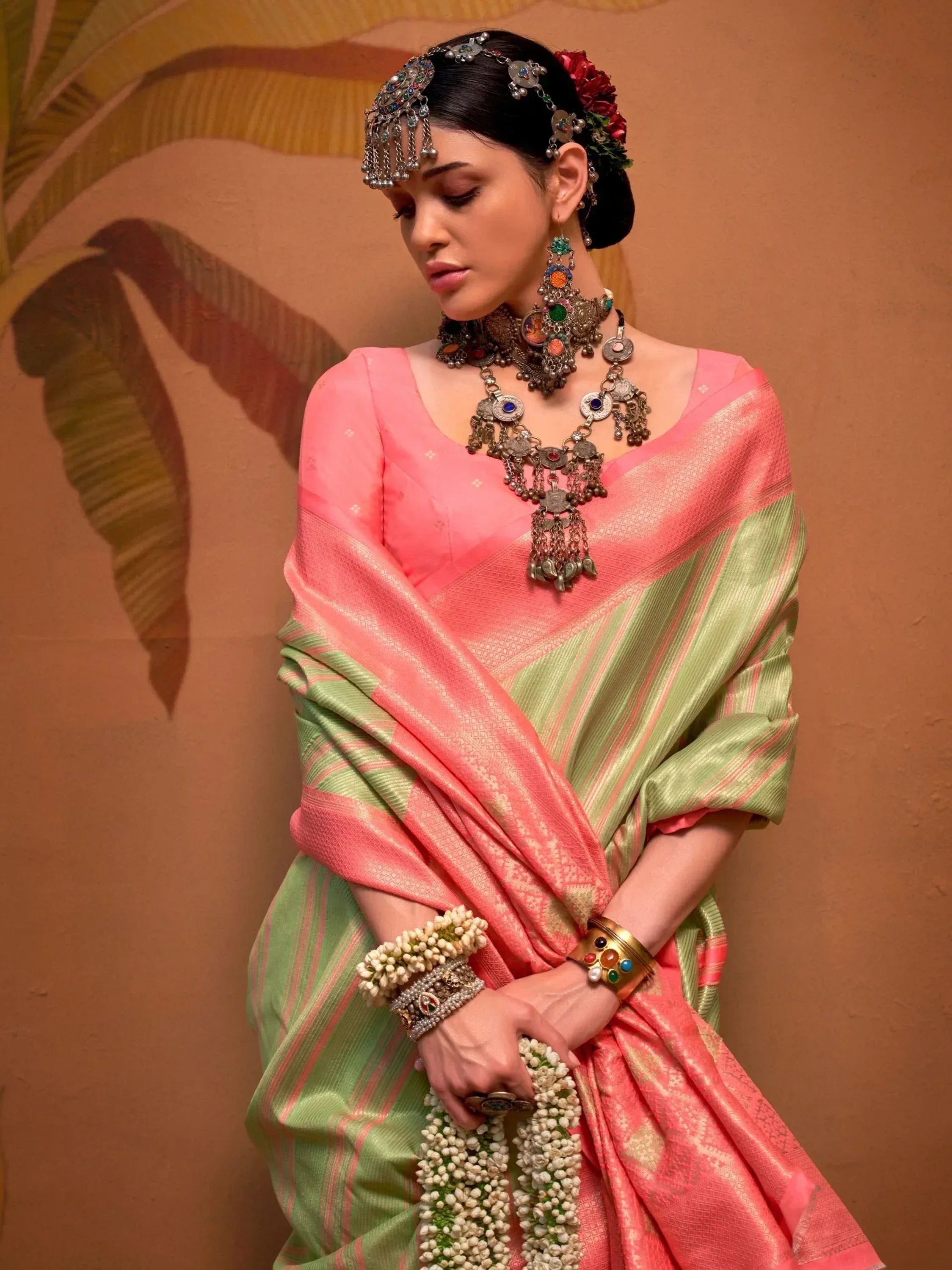 Woman in pink and green ethnic saree with traditional jewelry and floral accessories