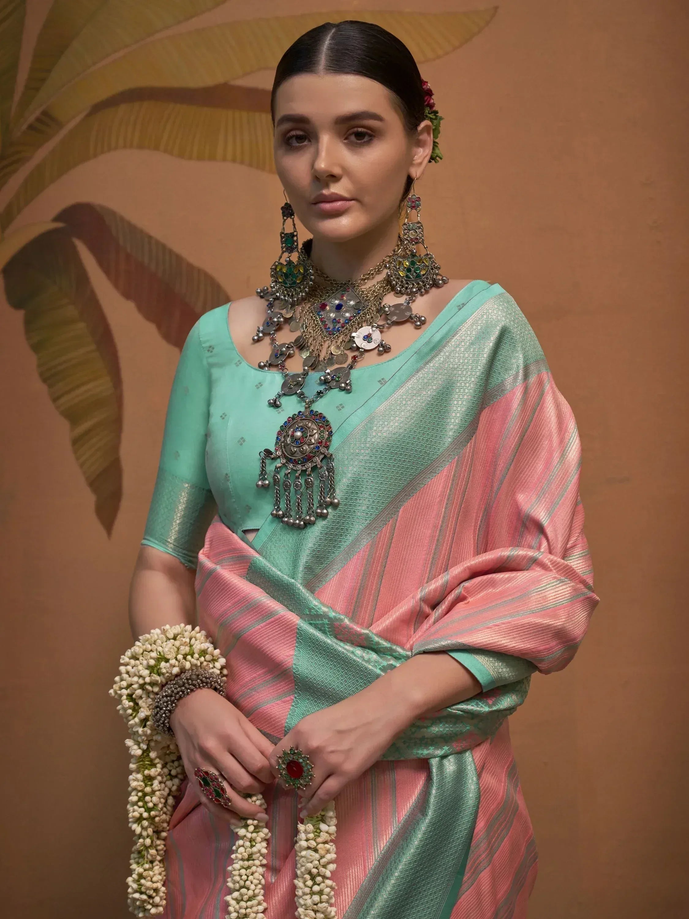 Elegant woman in mint and pink saree with traditional jewelry and floral garland