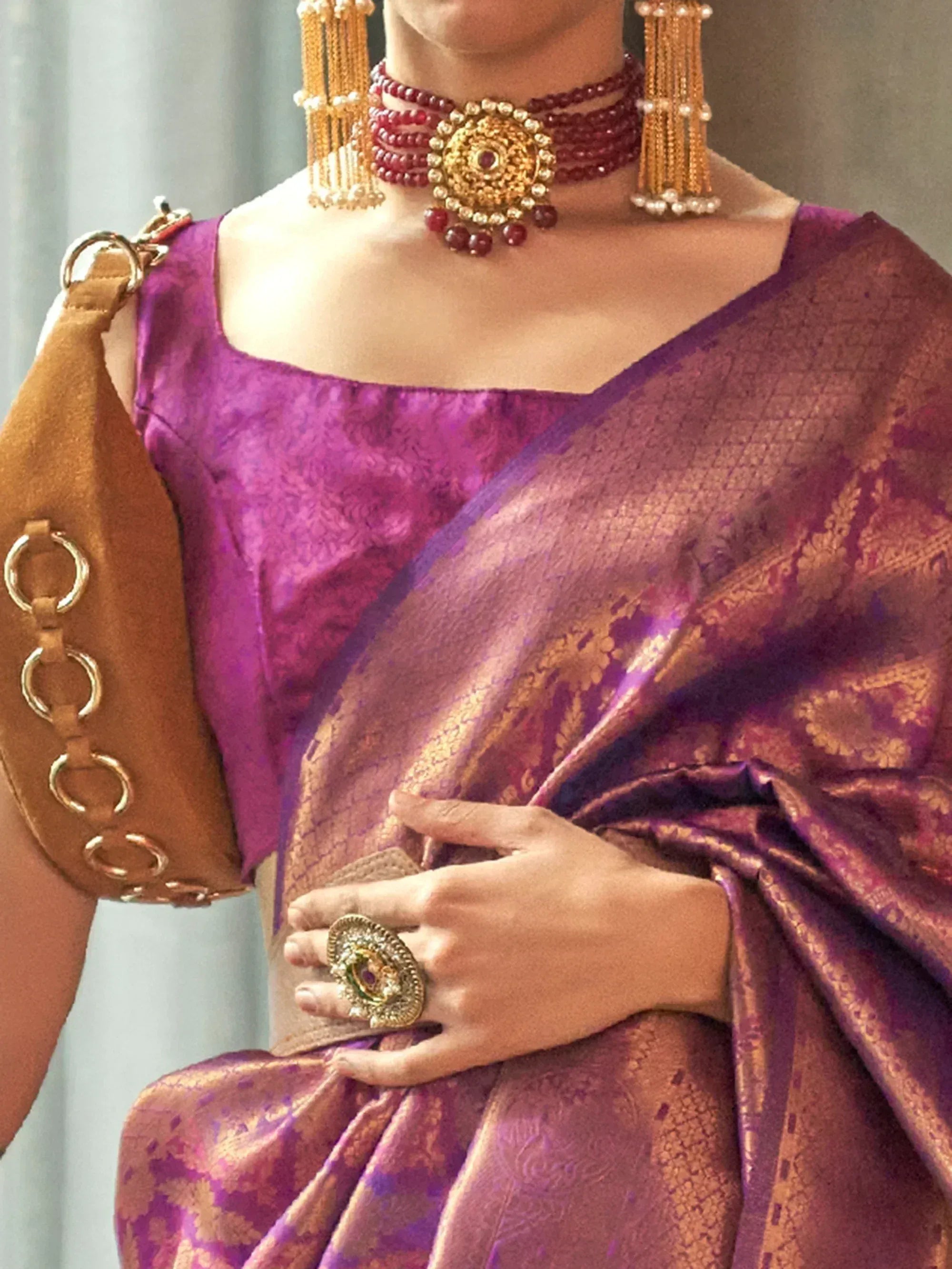 Purple silk saree with gold embroidery, paired with traditional Indian jewelry and a brown clutch bag.