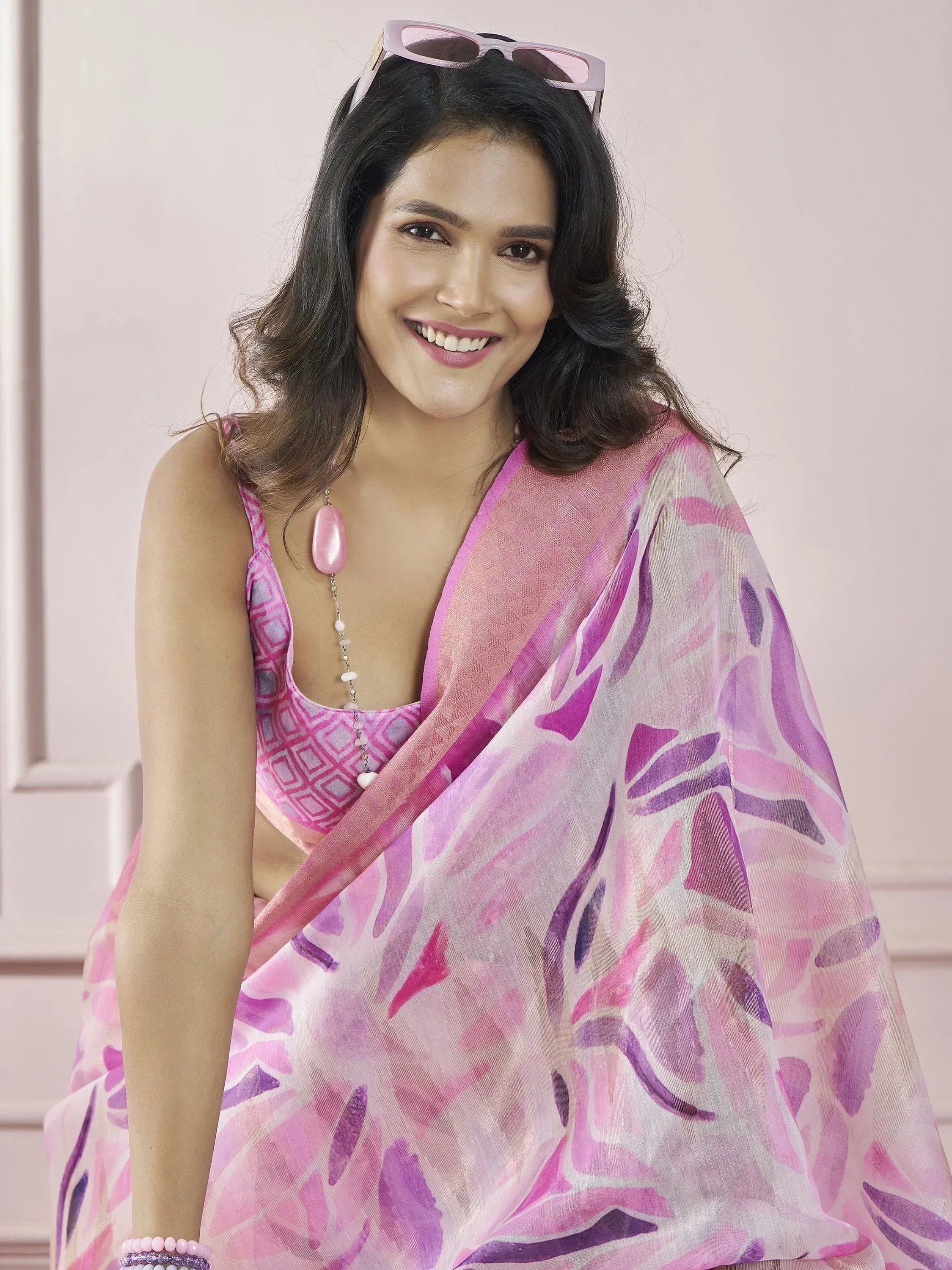 Woman in pink floral printed saree with matching blouse, stylish sunglasses, and pearl jewelry