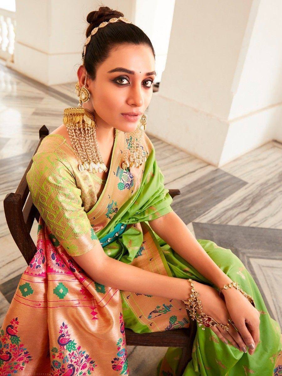 Woman in vibrant green and gold embroidered saree with traditional Indian jewelry, seated elegantly