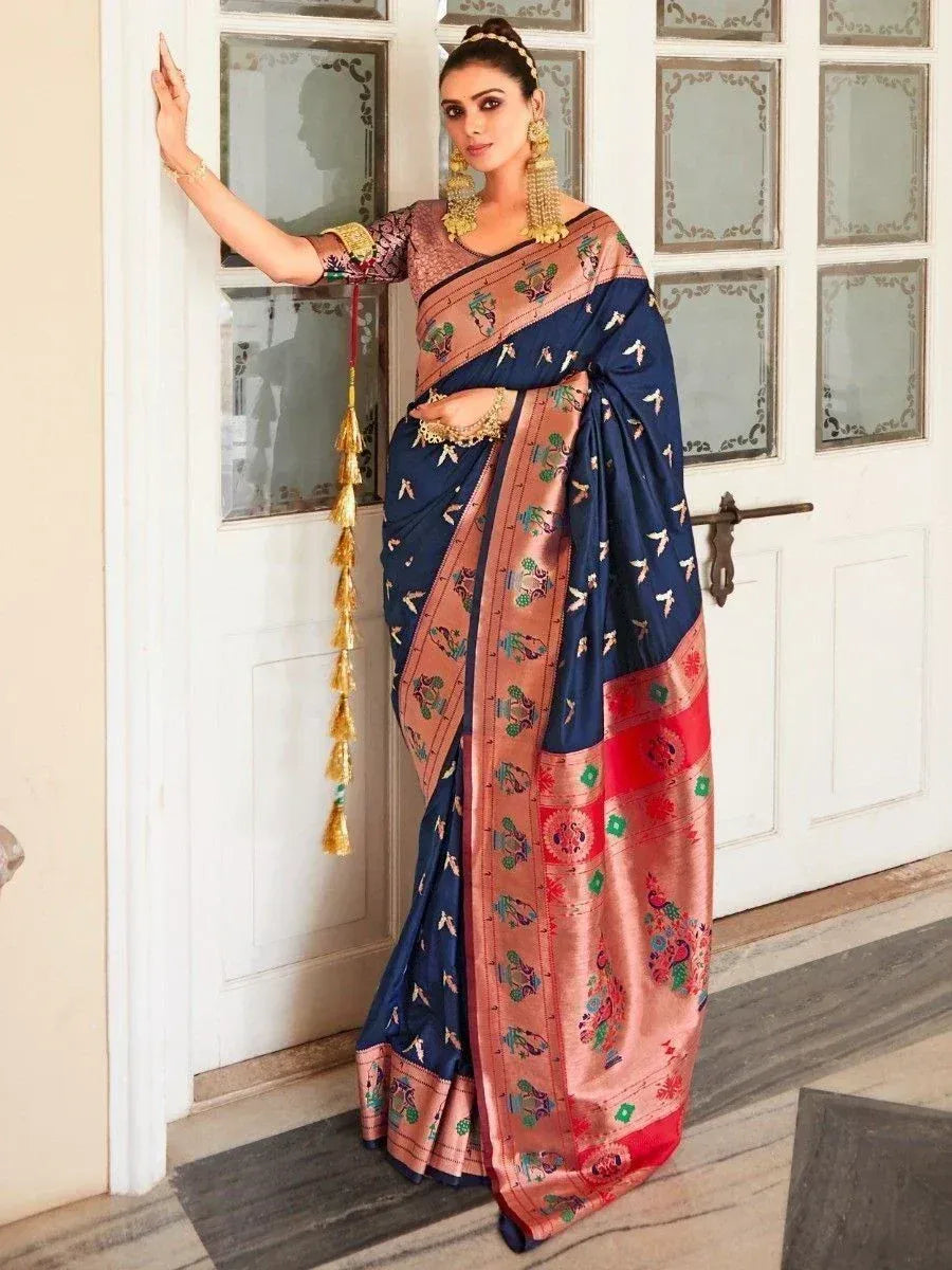 Woman in navy blue and peach designer saree with floral motifs, gold jewelry, standing by ornate door